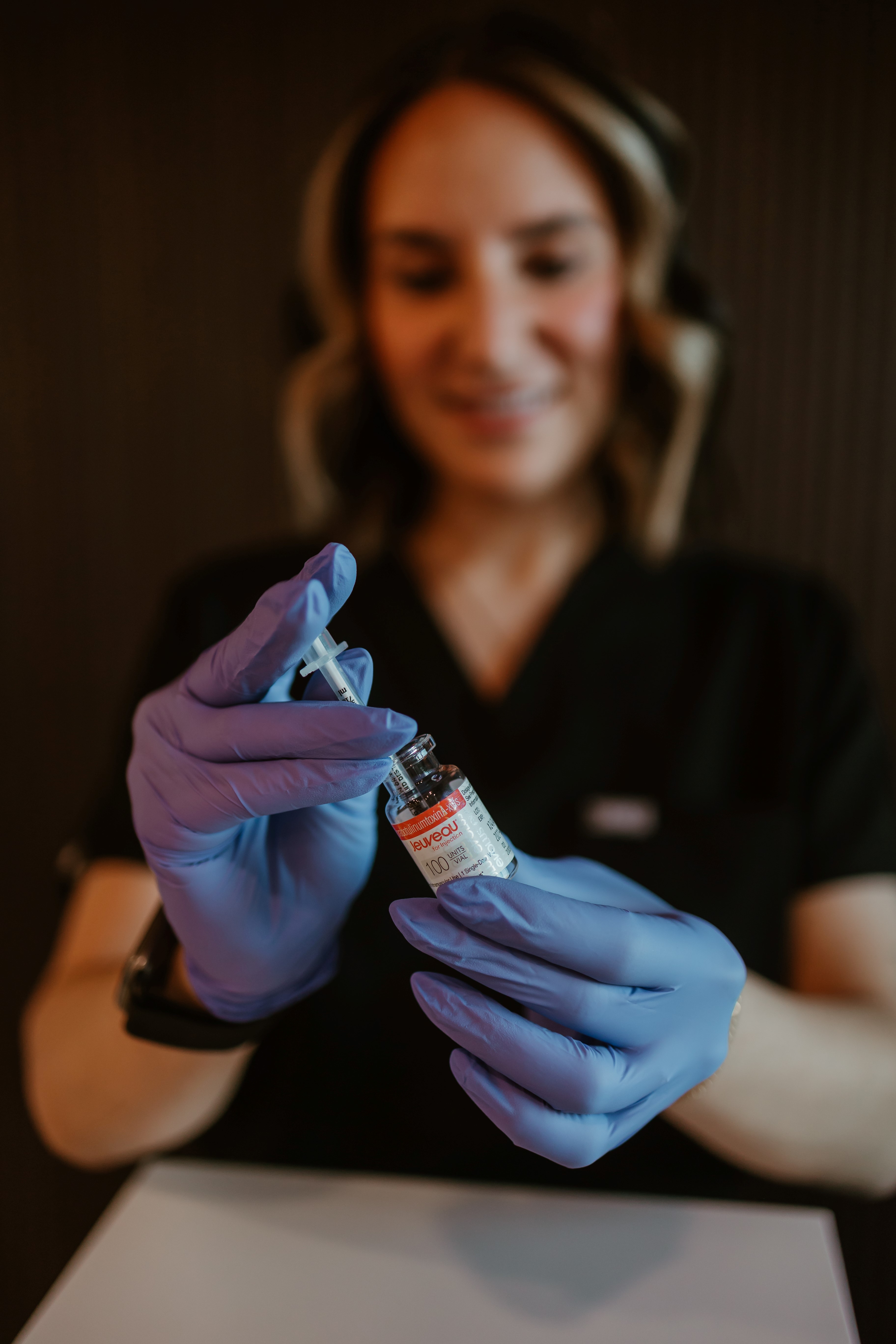 Person wearing blue gloves holding a syringe and a vial labeled Jeuveau, preparing an injection.