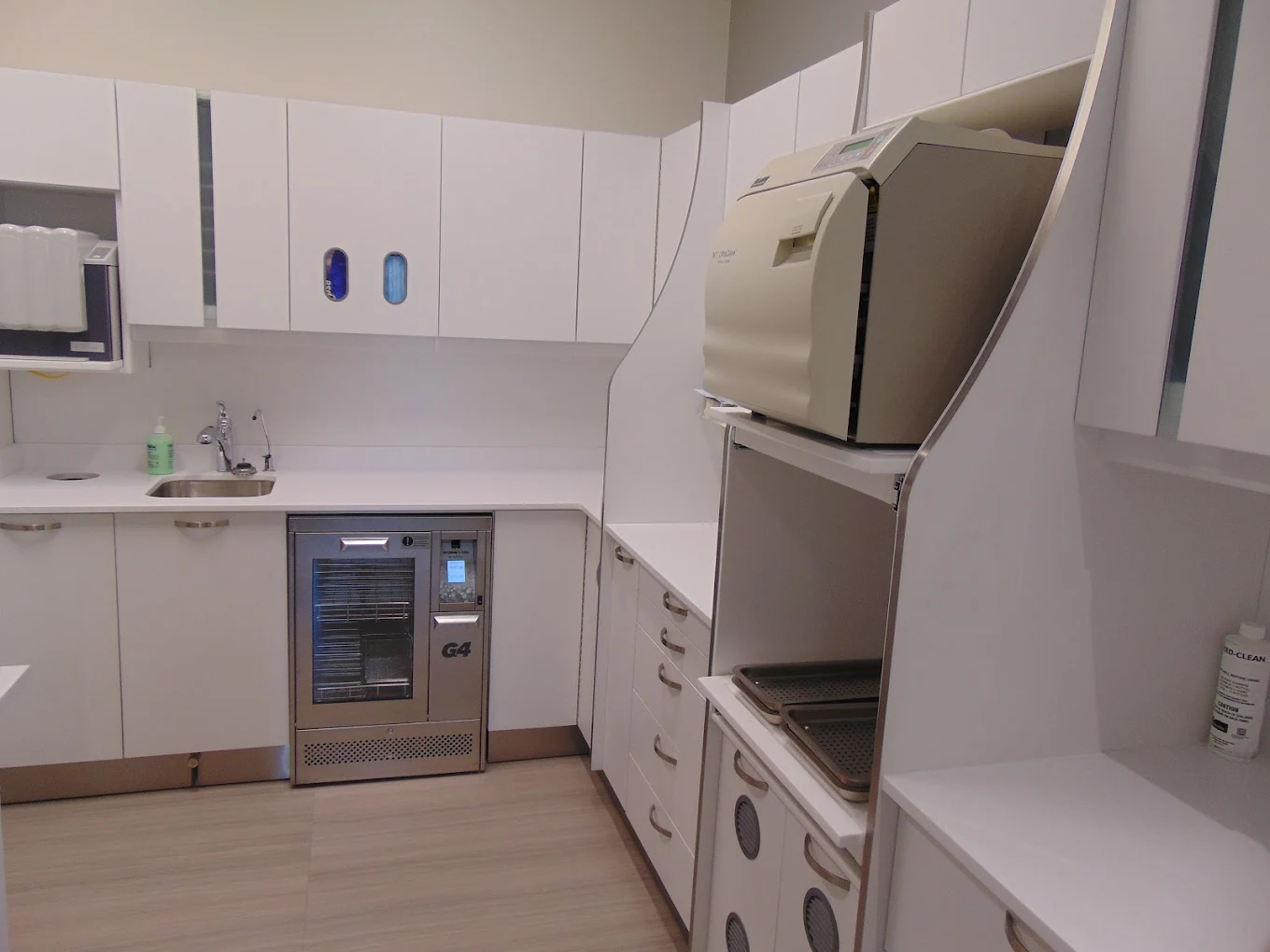 Clean, modern sterilization room with white cabinets, stainless steel sterilizer, and a small sink.