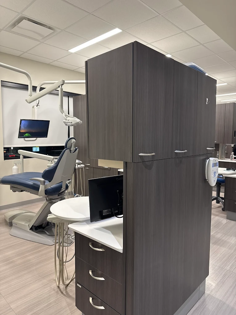 Modern dental office with a dental chair, overhead light, monitor, and cabinetry for tools and supplies.