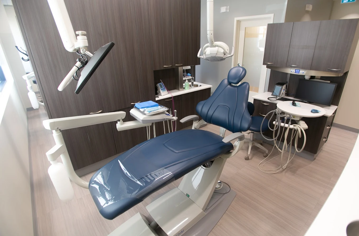 Modern dental operatory with a blue patient chair, overhead light, tools, and cabinetry.