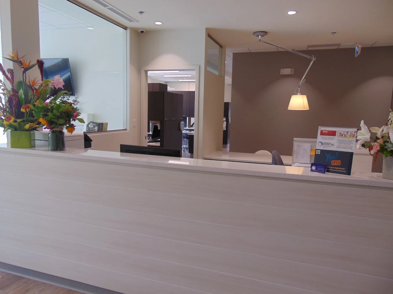 Reception area with white counter, floral arrangements, informational signs, and an open office doorway.