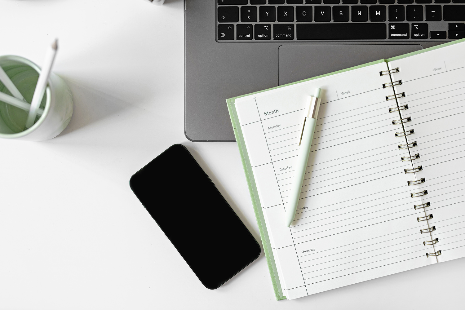Planner and phone on a light green workspace