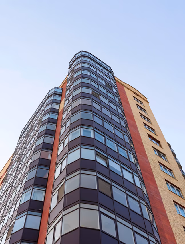Low-angle view of a modern high-rise building with glass panels and brick walls against a clear sky.