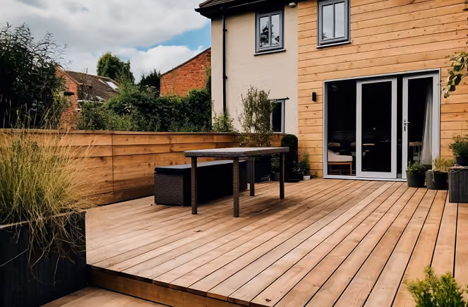 Wooden deck patio with table, bench, and sliding glass door leading into a house.