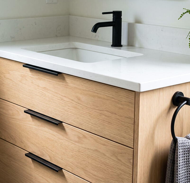 Modern bathroom with a white freestanding tub, wooden bench, mannequin with hat, and large window.