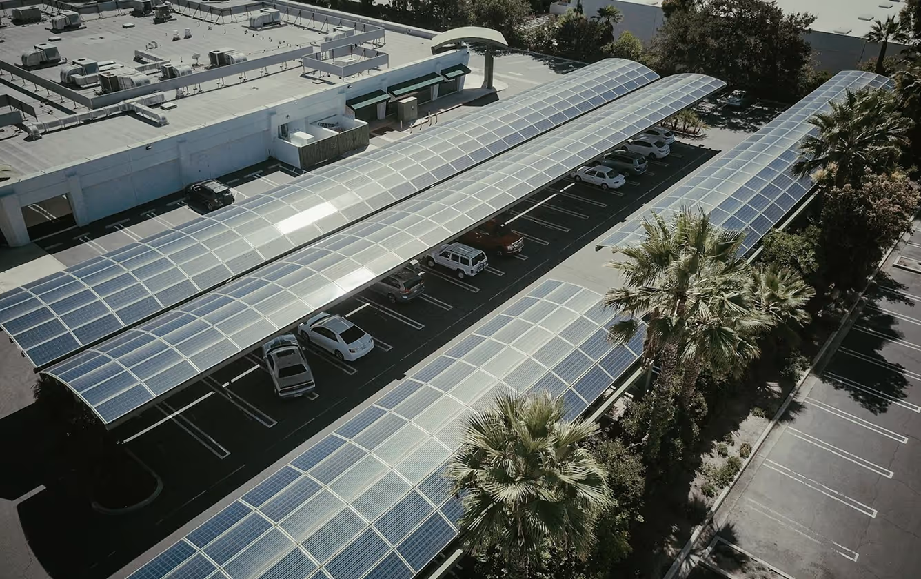 Aerial view of a parking lot with solar panel canopies covering parked cars and surrounded by palm trees.