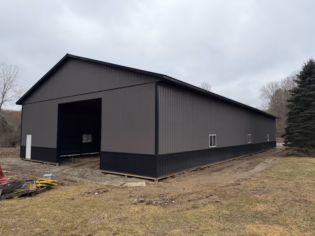Large gray and black metal storage building without doors in a grassy area under a cloudy sky.