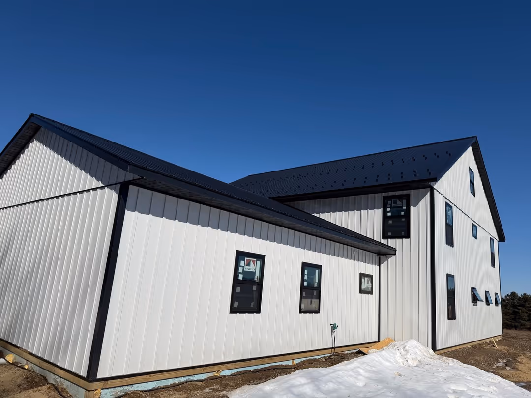 Newly constructed modern white building with black roof and multiple dark-framed windows under a clear blue sky.