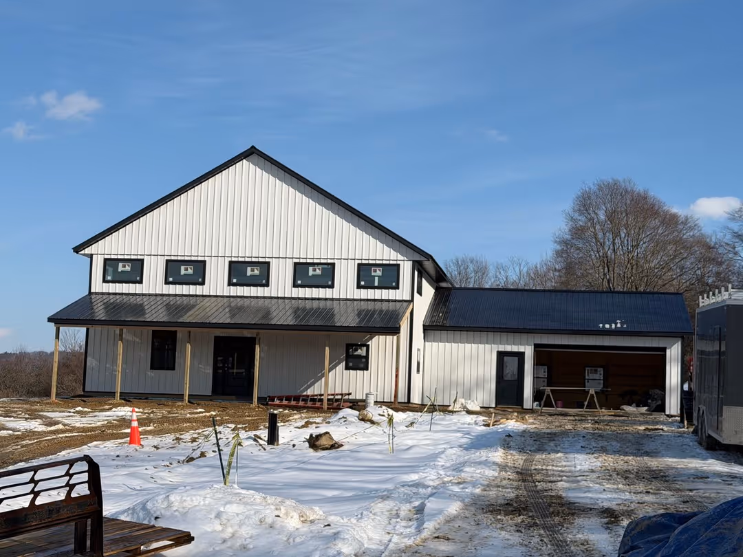 A modern two-story white house with black roof under construction on a snowy ground with clear blue sky.