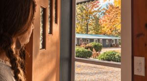 Guest looking out from a Lakeside Heritage Resort room toward colorful autumn trees and the resort grounds in Northern Michigan.