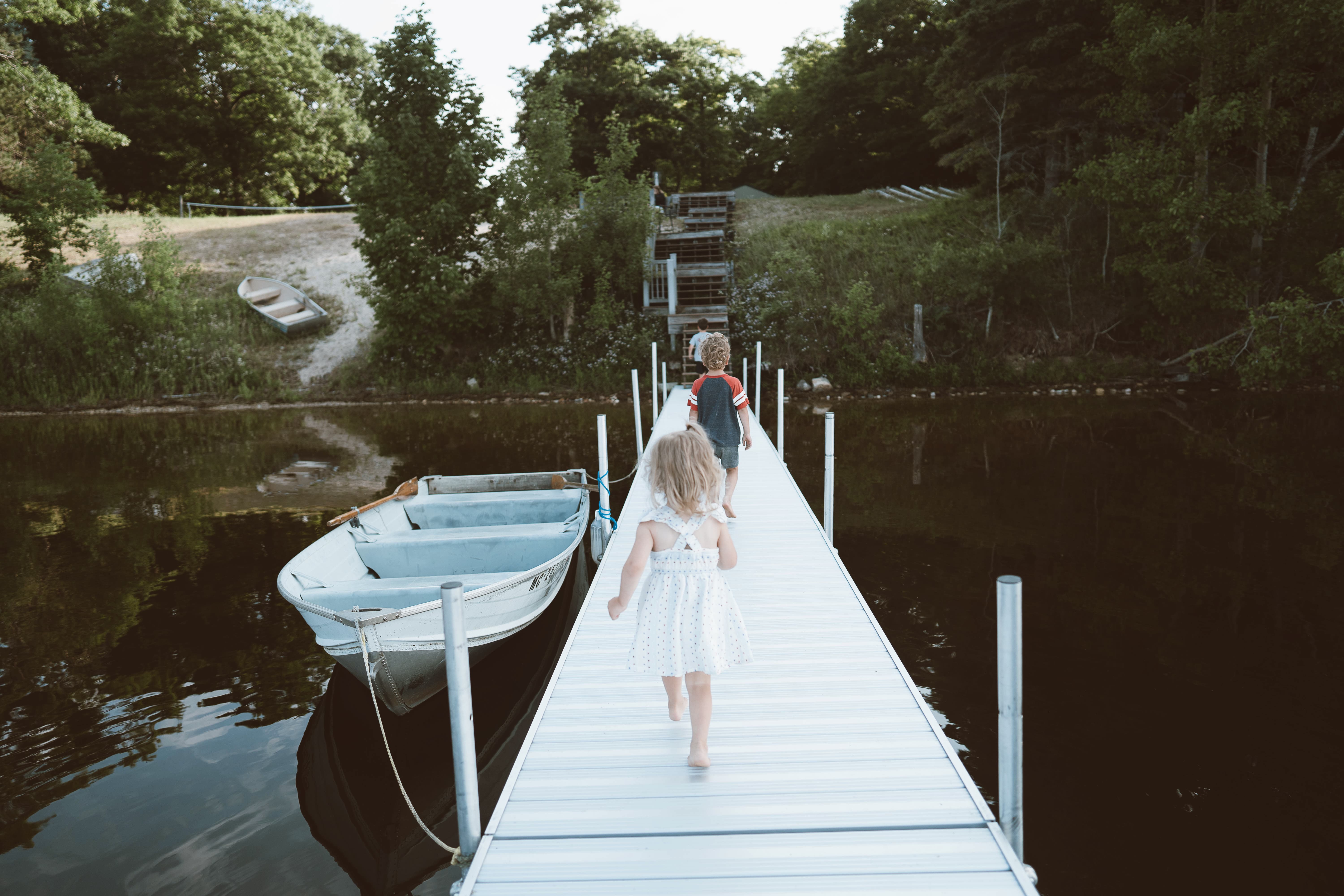 Children walking along a lakeside dock beside a rowboat during a summer vacation in Northern Michigan.