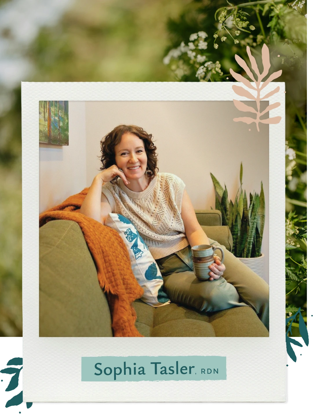 Sophia Tasler lounging on green couch holding a mug, next to a plant and orange blanket.