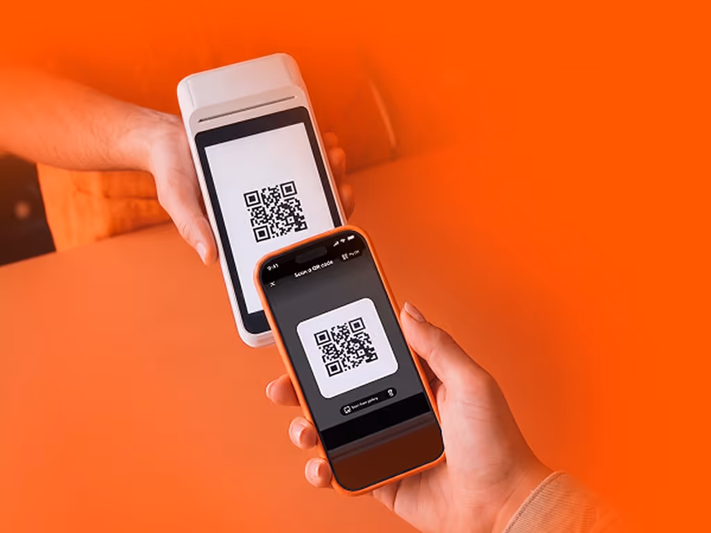 Mano sosteniendo un teléfono con código QR frente a un lector QR, representando un pago con Mi Clip, la app de pagos.