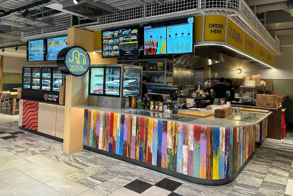 Colorful sushi restaurant counter with digital menu screens and a bronze elephant logo sign.