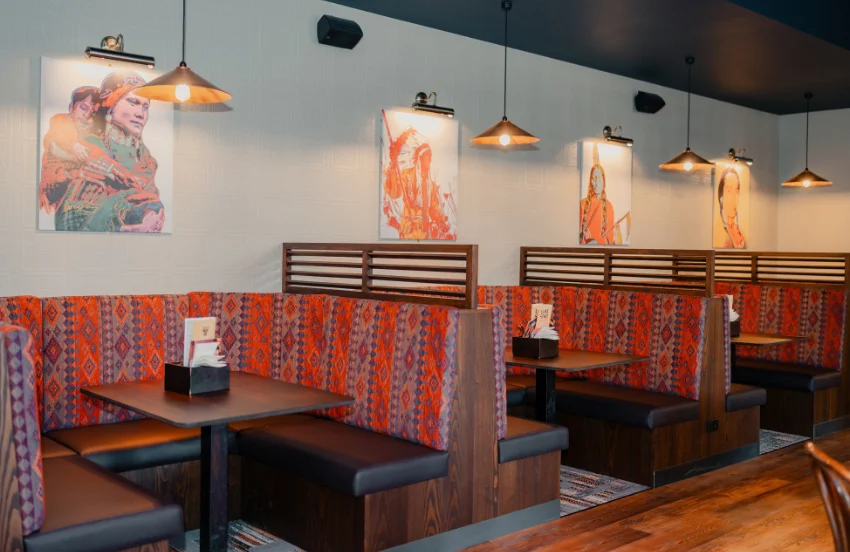 Restaurant booths with patterned red cushions, warm lighting, and colorful artwork on light gray walls.
