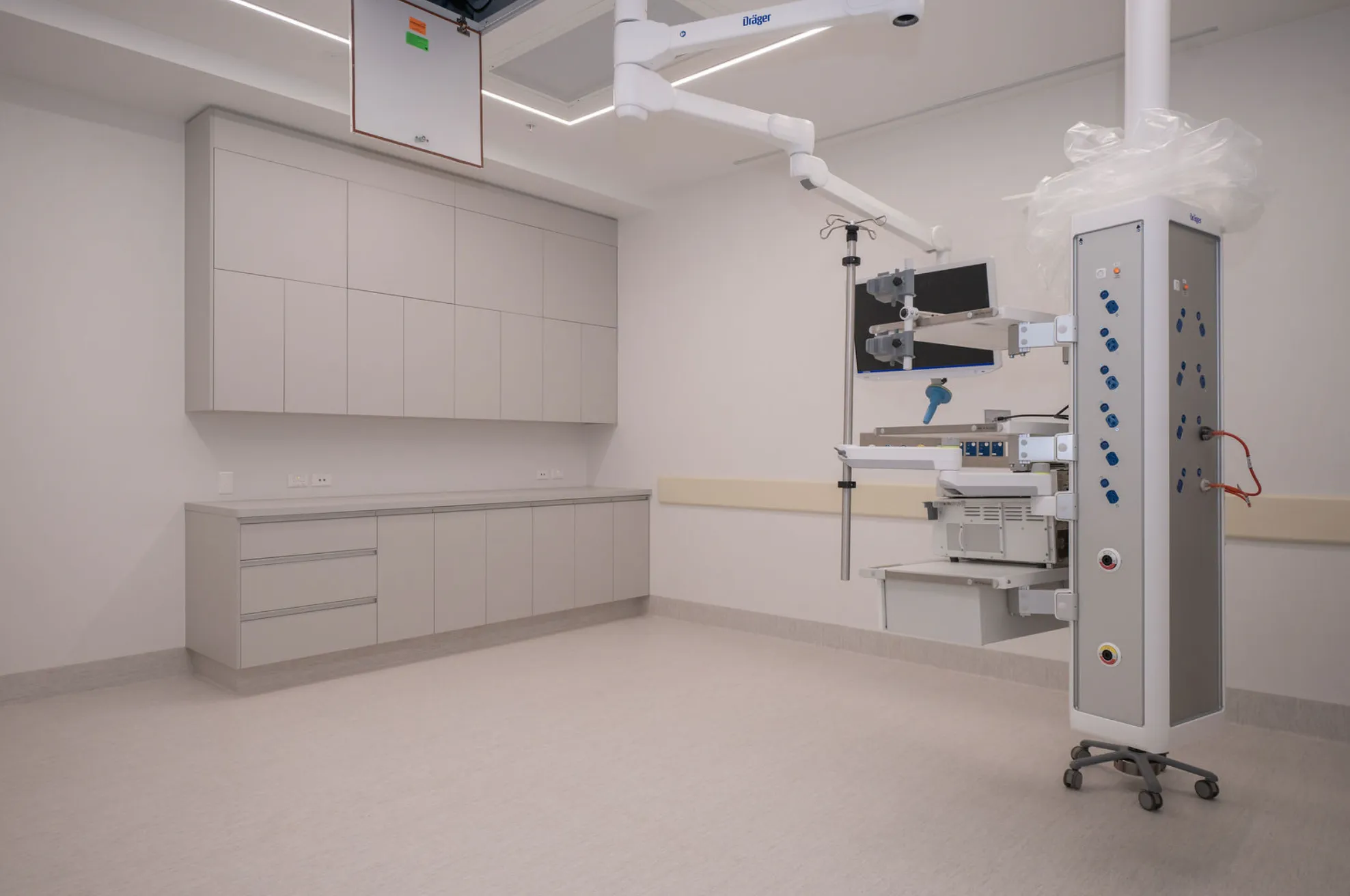 Empty hospital room with medical equipment, cabinets, and clean beige floor and walls.