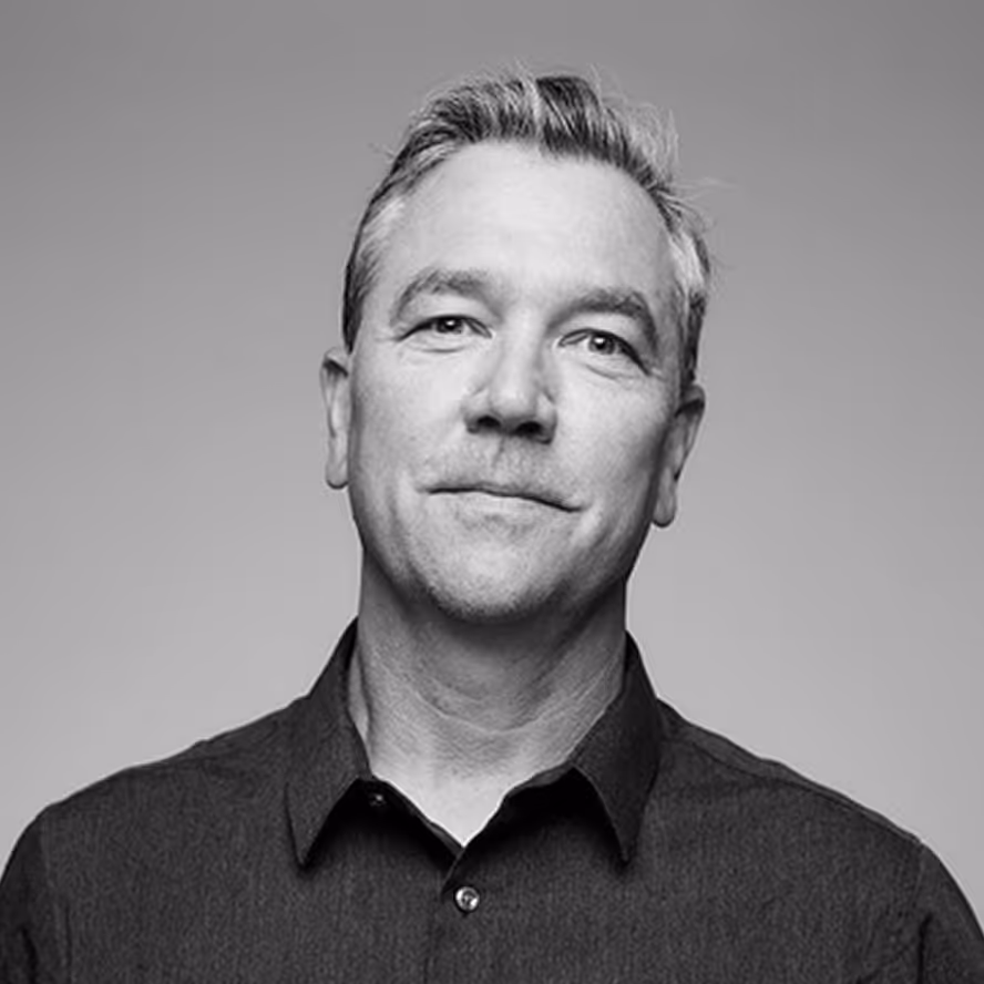 Black and white headshot of a middle-aged man with short hair wearing a dark button-up shirt.