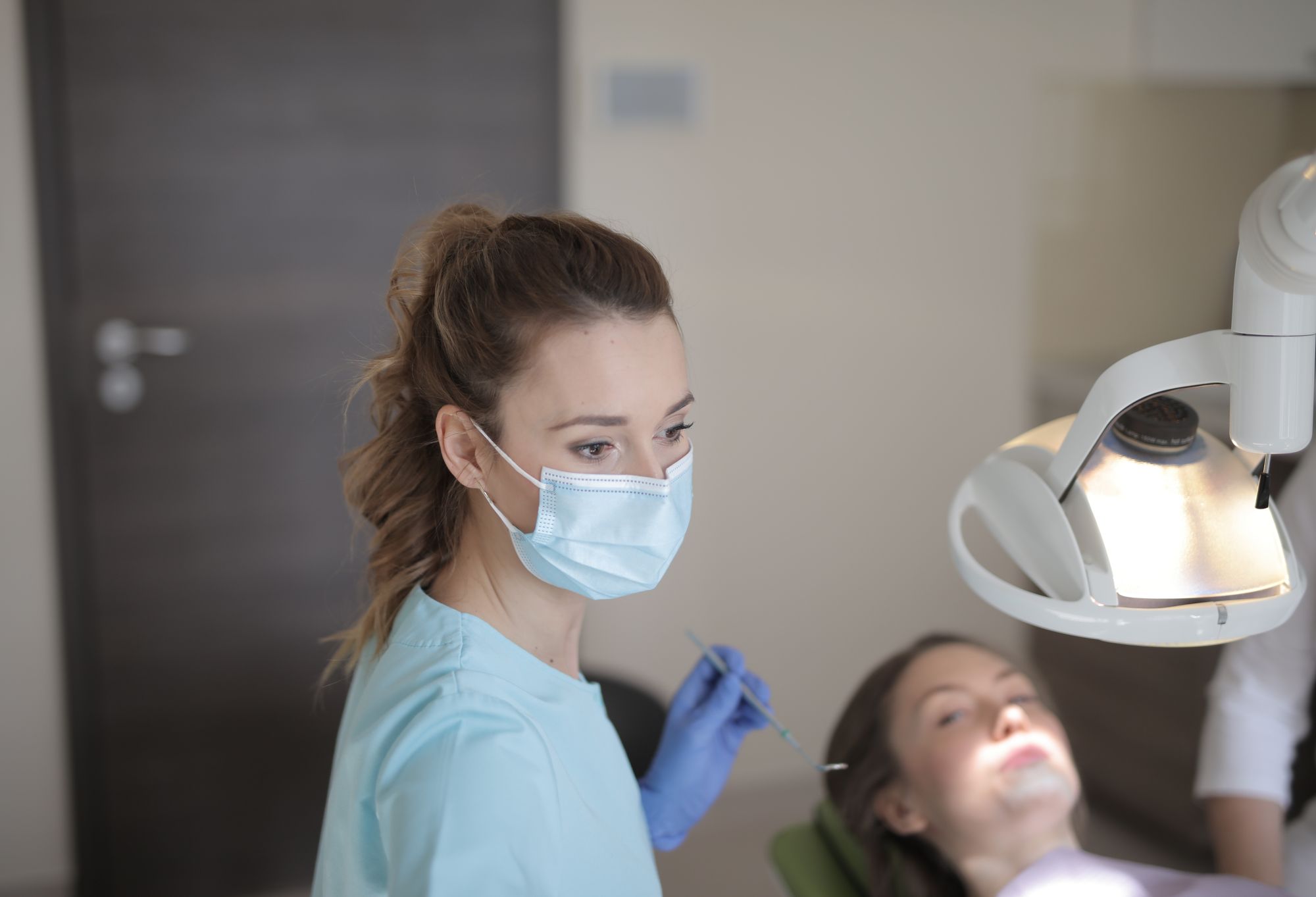 Dentist in a mask and gloves treating a patient under the dental light in a clinic