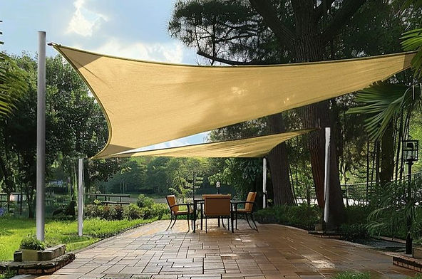 Tan shade sails over a patio with a table and chairs. Surrounded by lush greenery and trees, creating a serene, inviting outdoor setting.