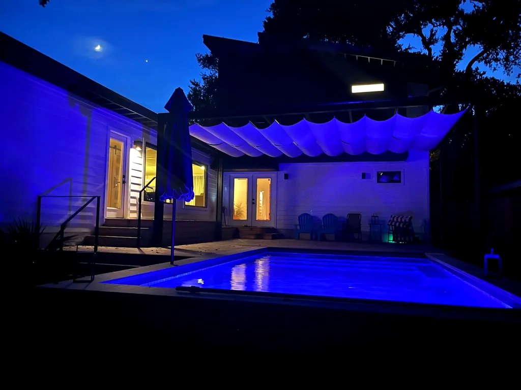 Sand-toned pergola shade glowing above the pool at night