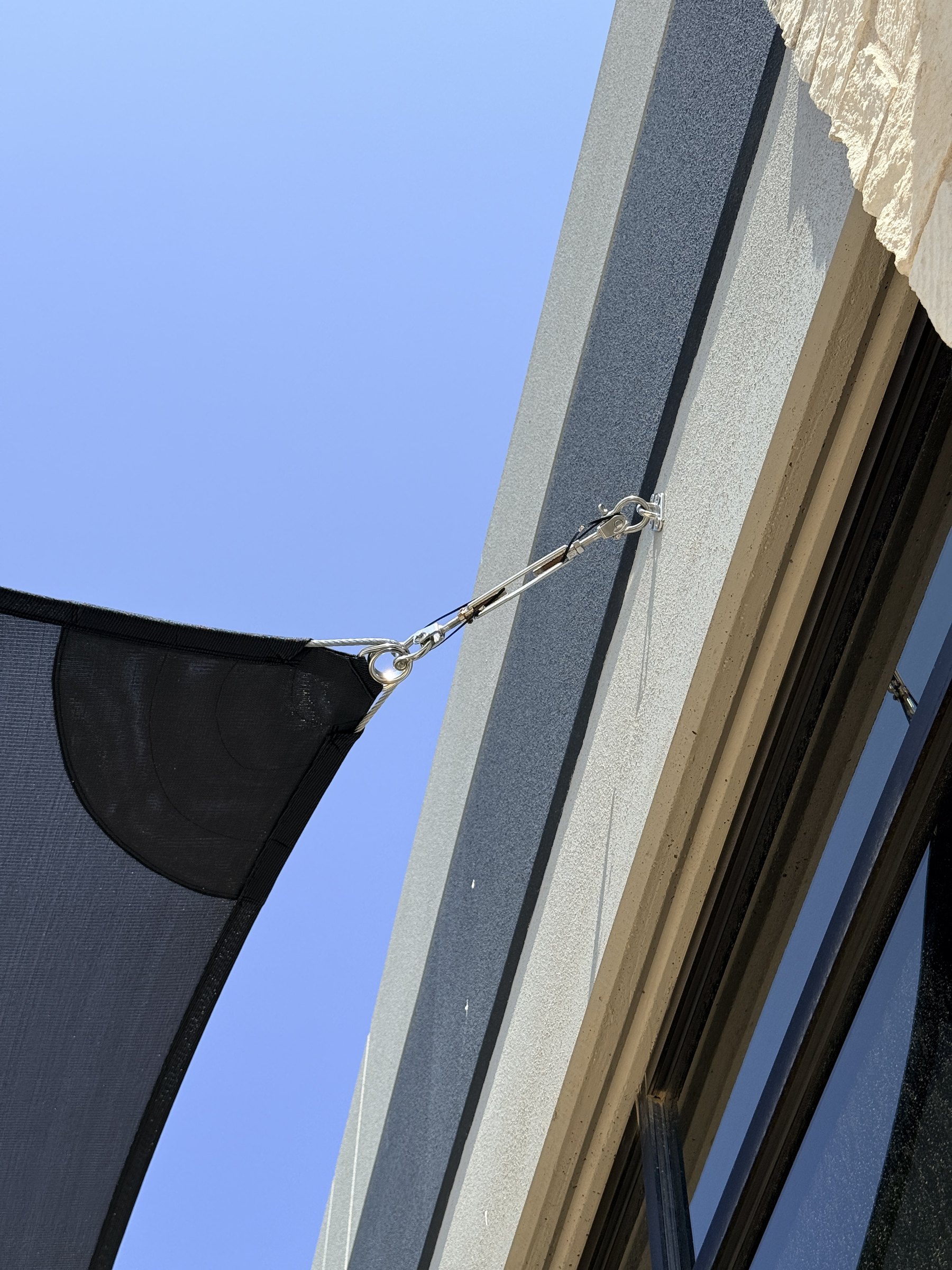 Close-up of a sail corner tensioned to the building with stainless hardware