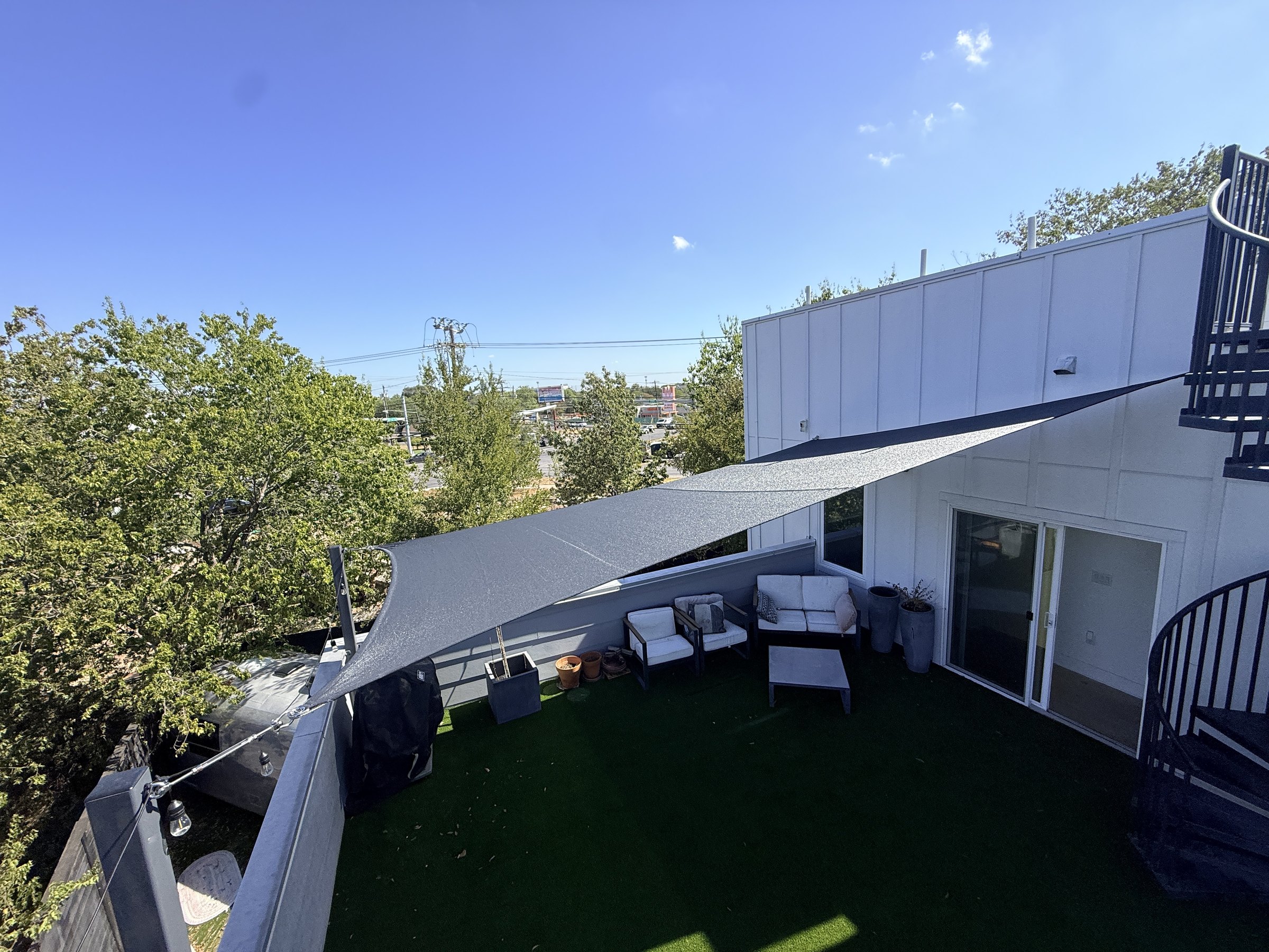 Charcoal four-corner sail over a rooftop turf terrace and lounge seating