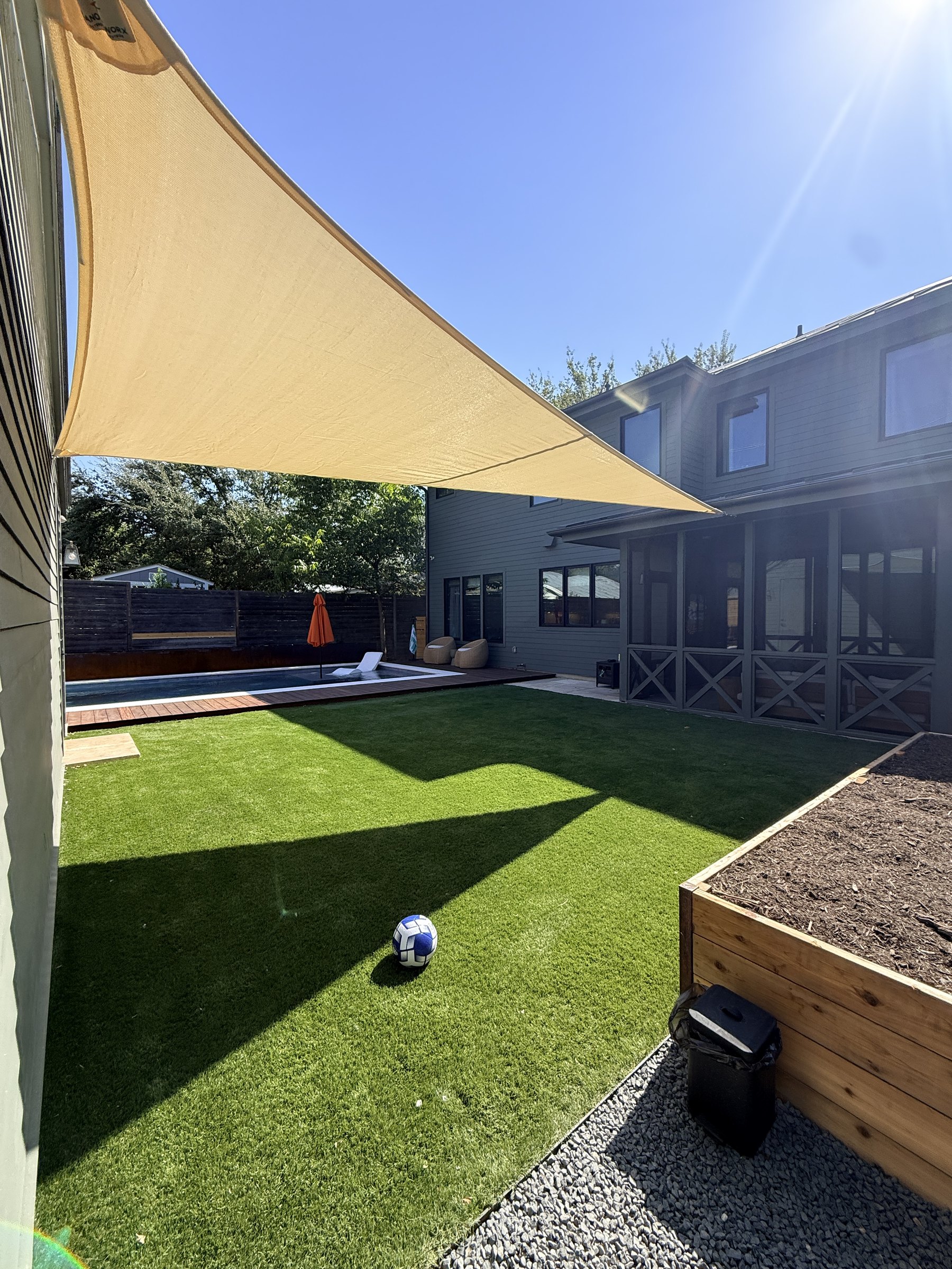 Natural-toned triangle sail shading the turf, with the pool beyond