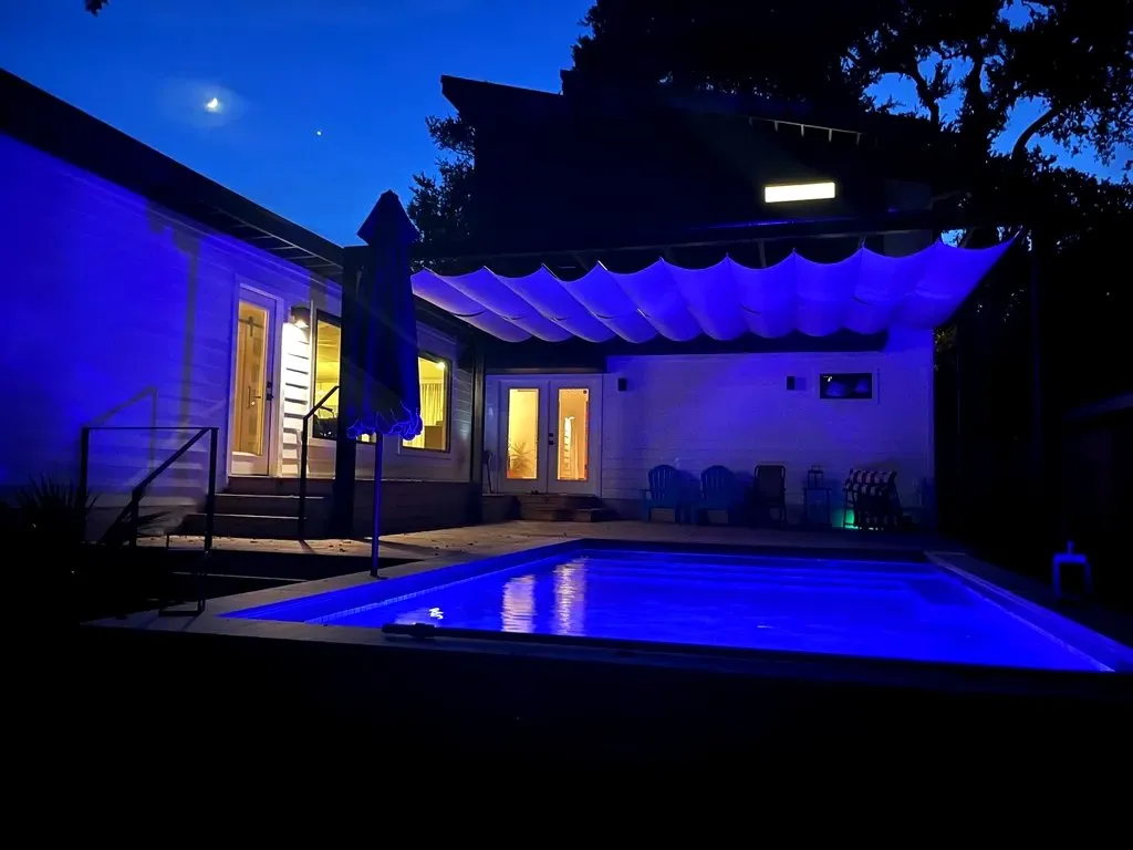 Sand-toned pergola shade glowing above the pool at night