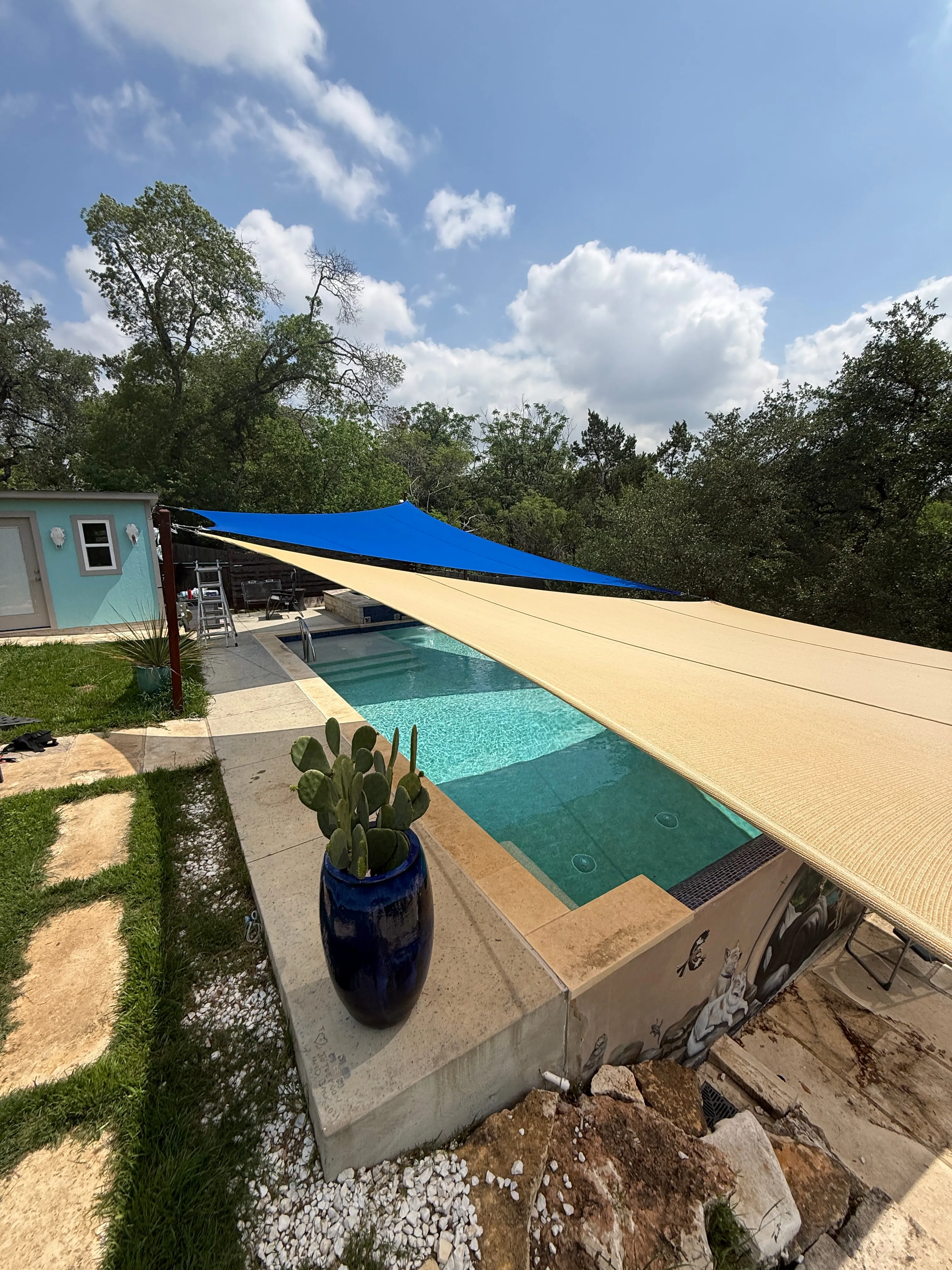 Sand and blue custom shade sails angled over a raised backyard pool in South Austin