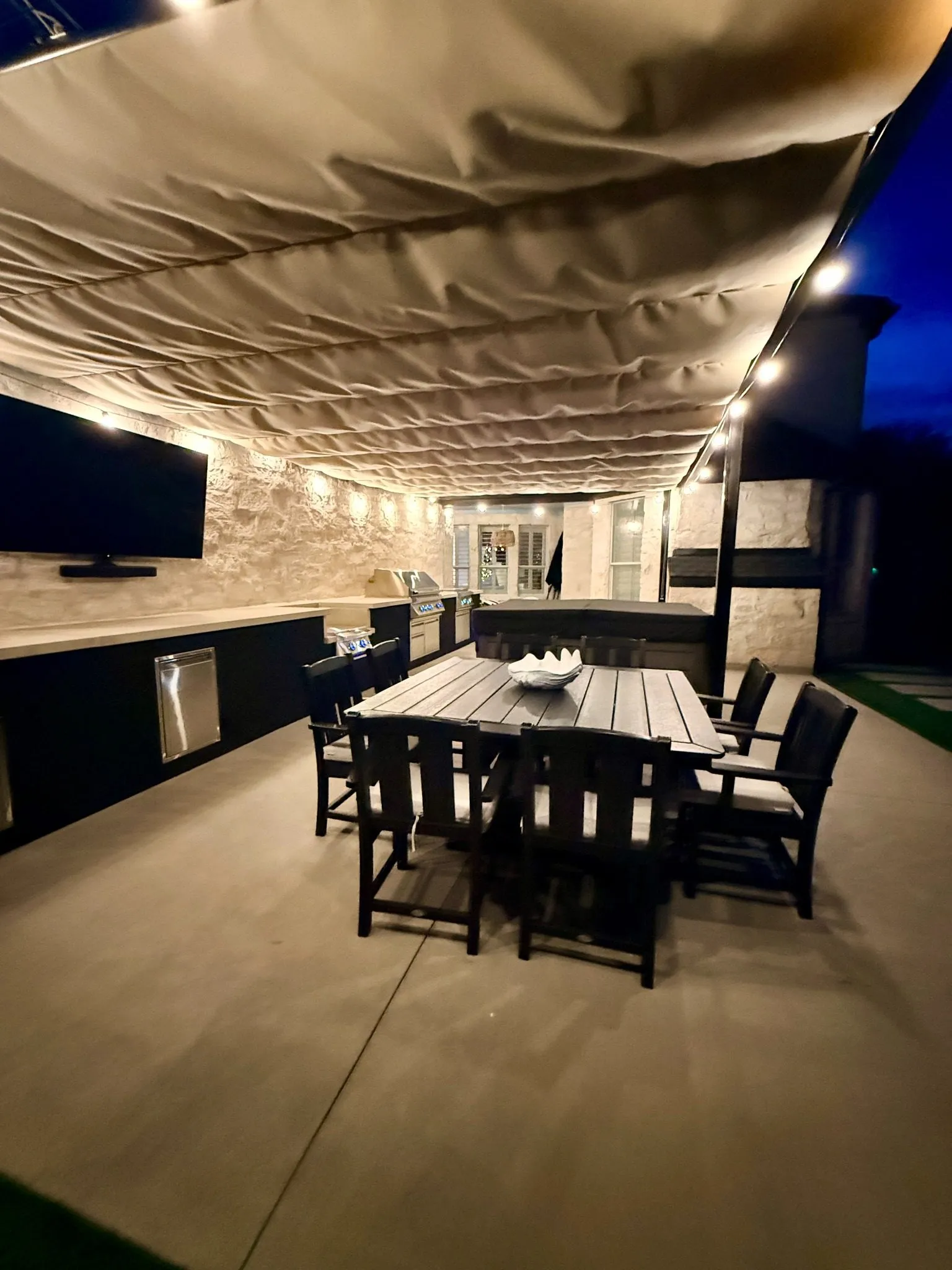 Under the extended Roman shade at night, looking along the outdoor kitchen