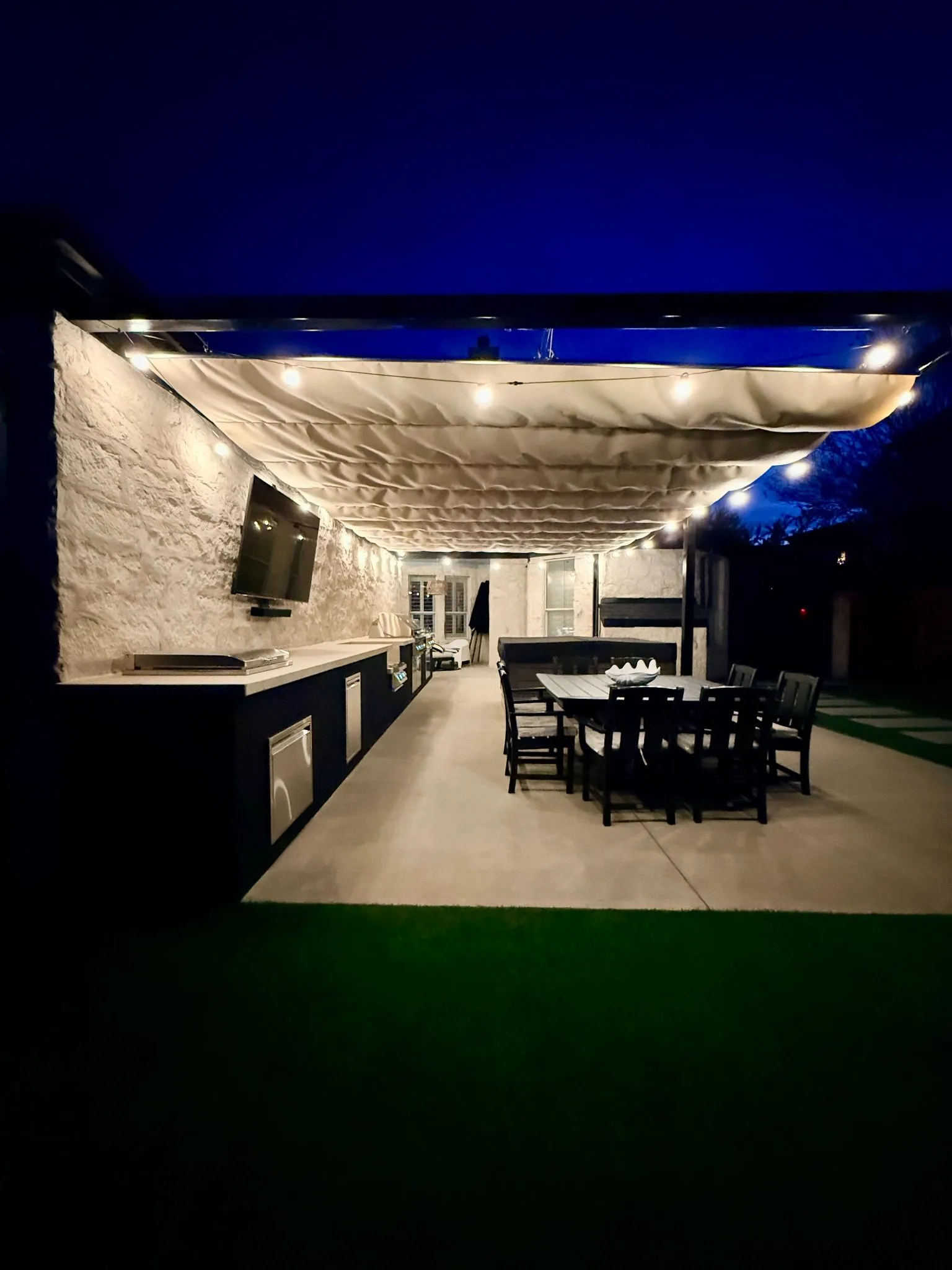 The full length of the Roman shade at night over the outdoor kitchen and dining area