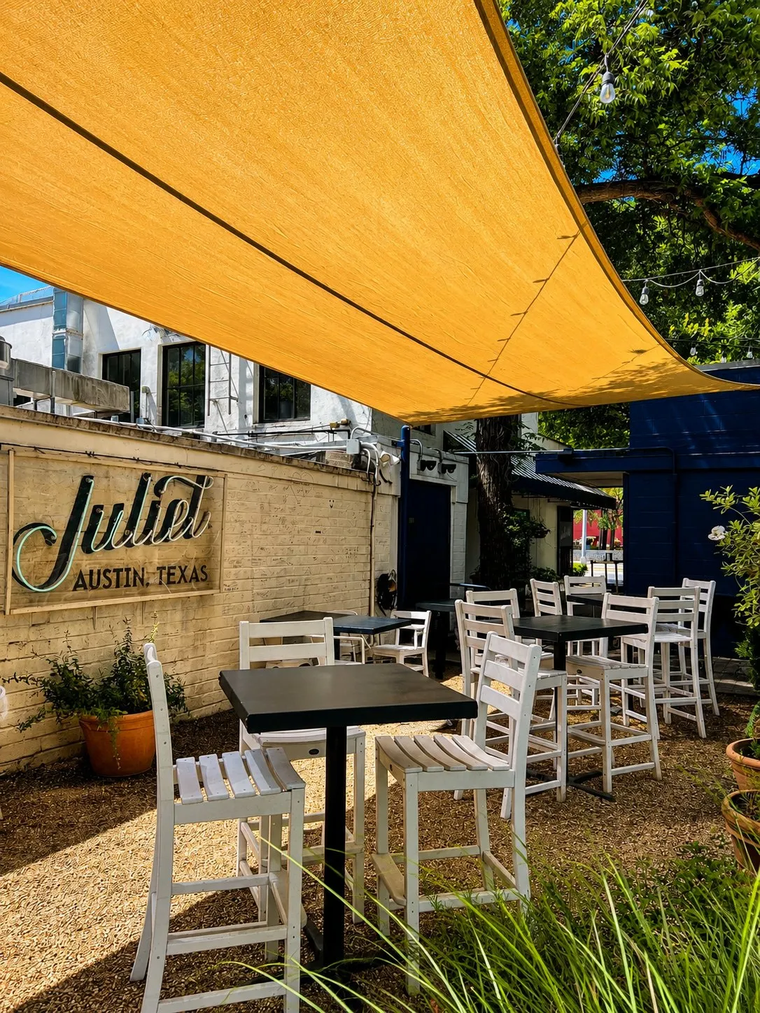 Yellow sail shading high-top tables and white chairs beside the Juliet sign