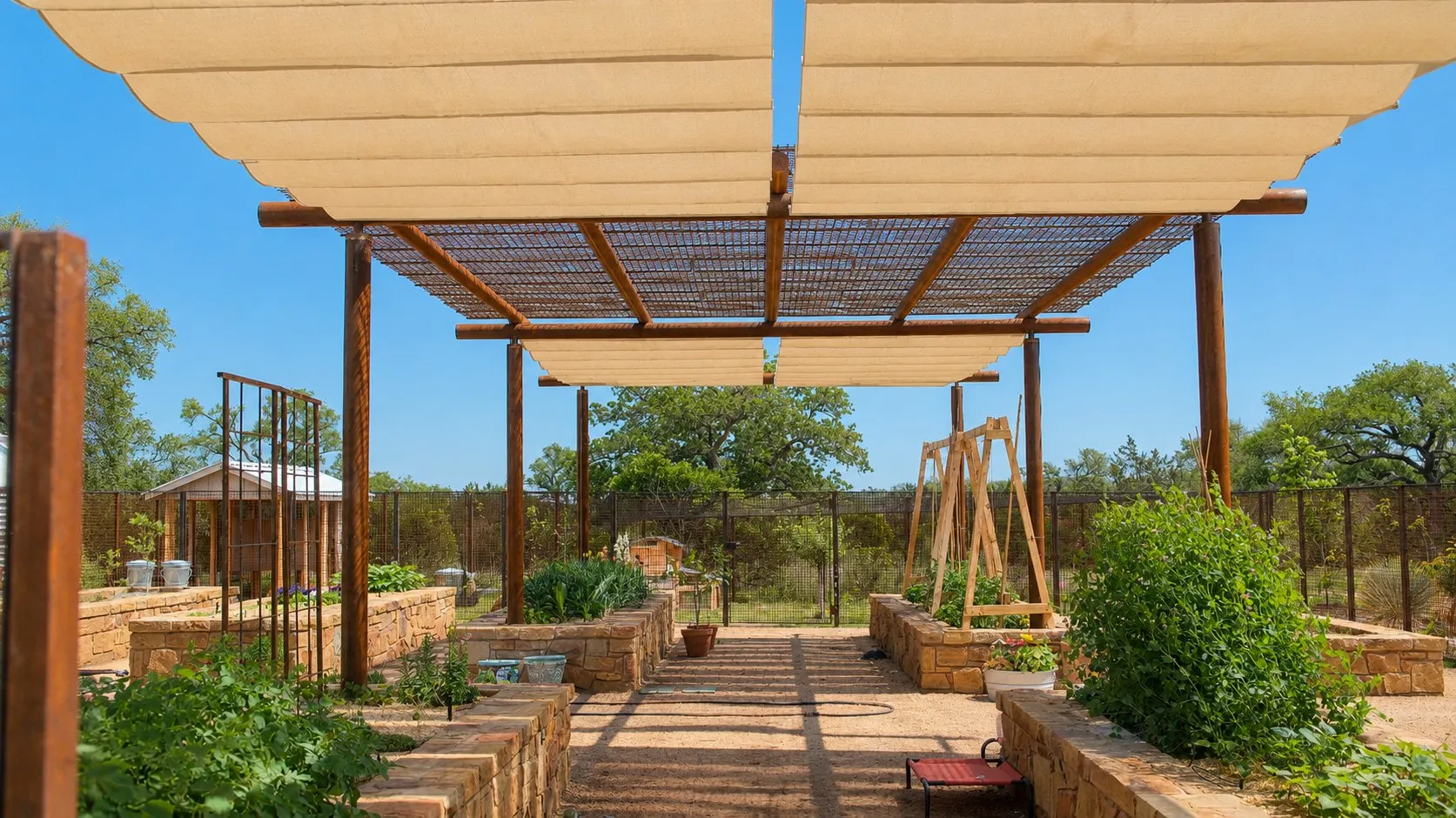 Roman shades extended on both sides of the pergola, with raised garden beds below