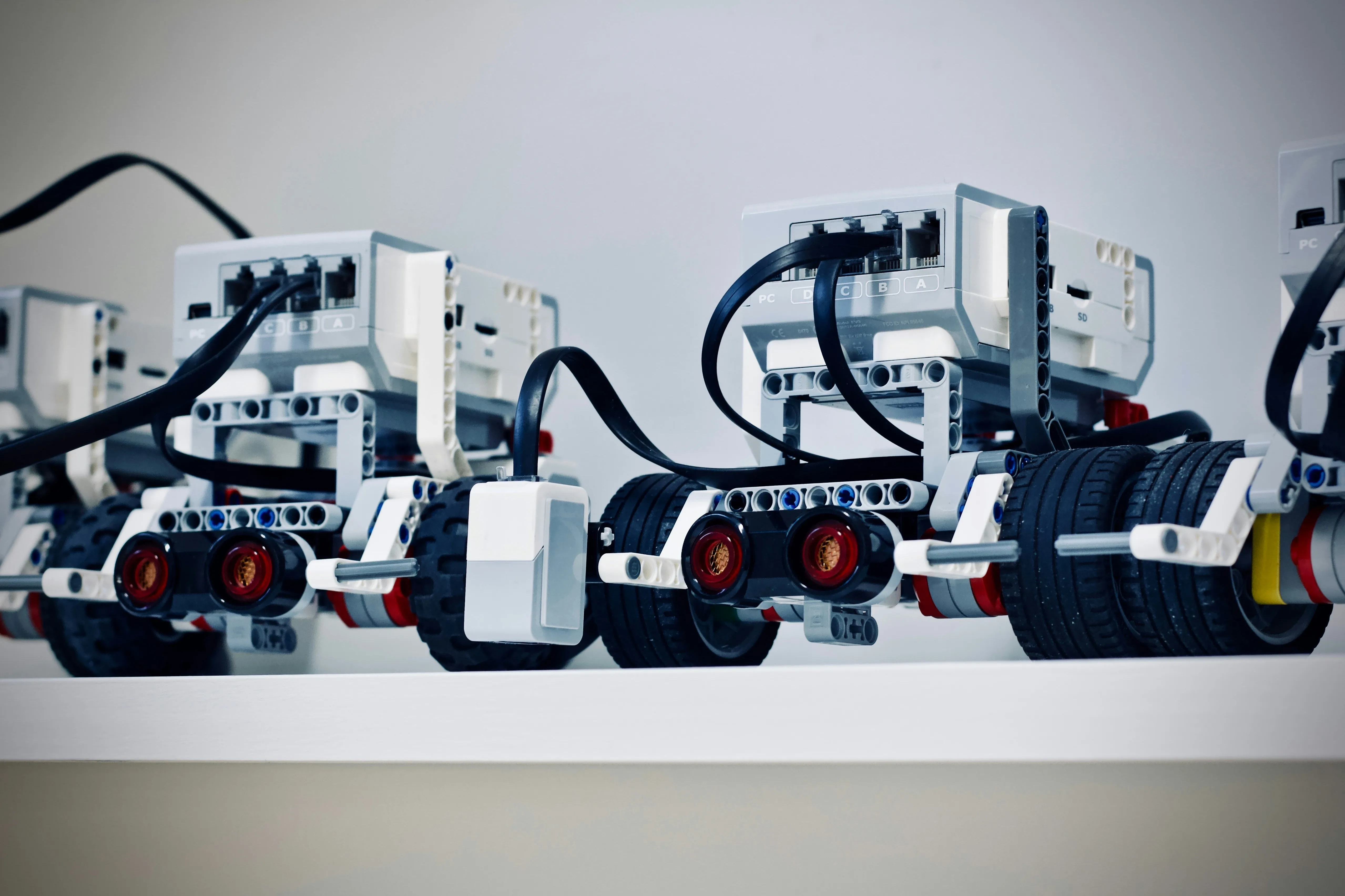 Close-up of small white and black robots with wheels and connected cables on a white surface.