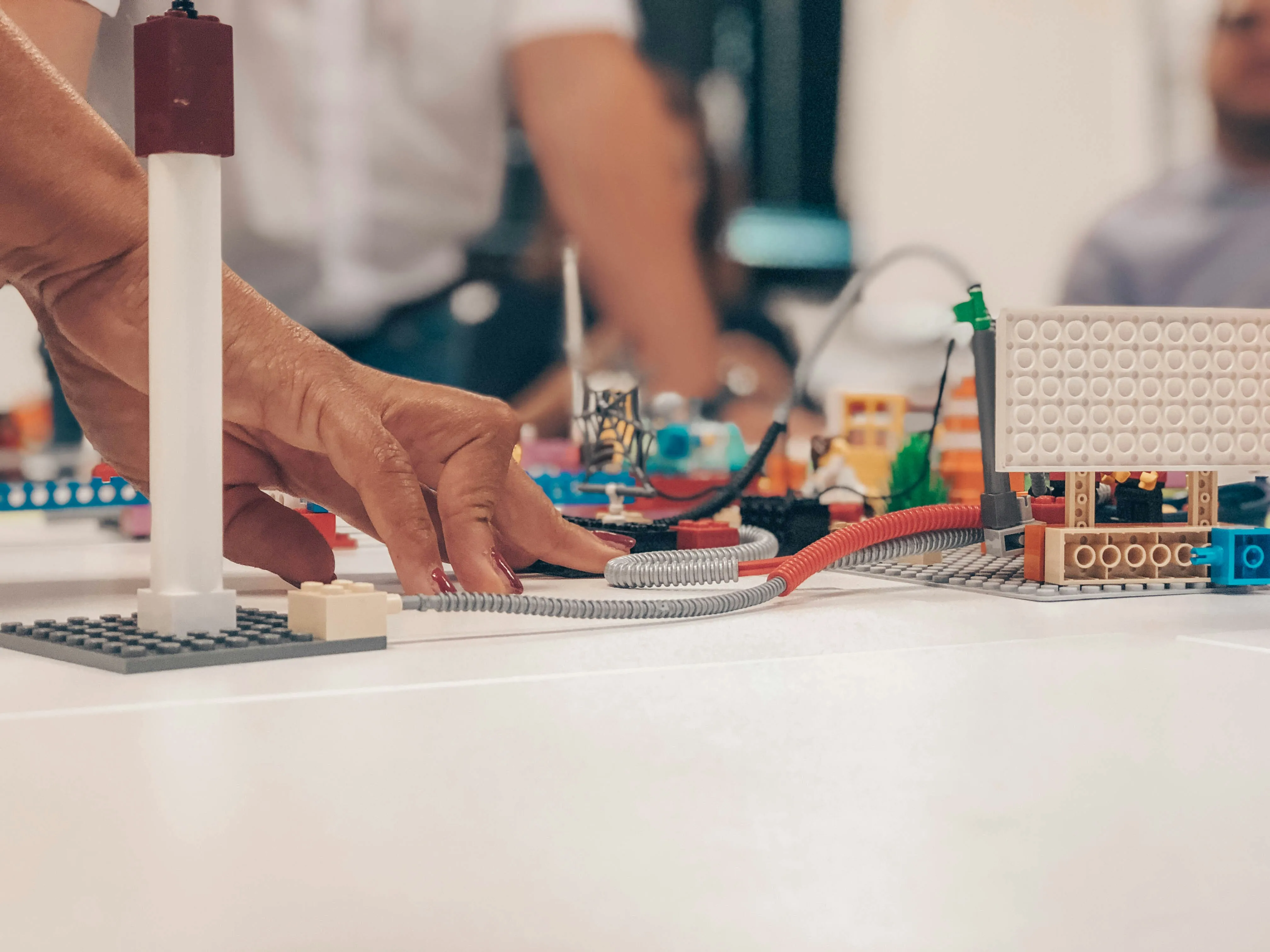Close-up of a hand interacting with a colorful LEGO building on a white table.