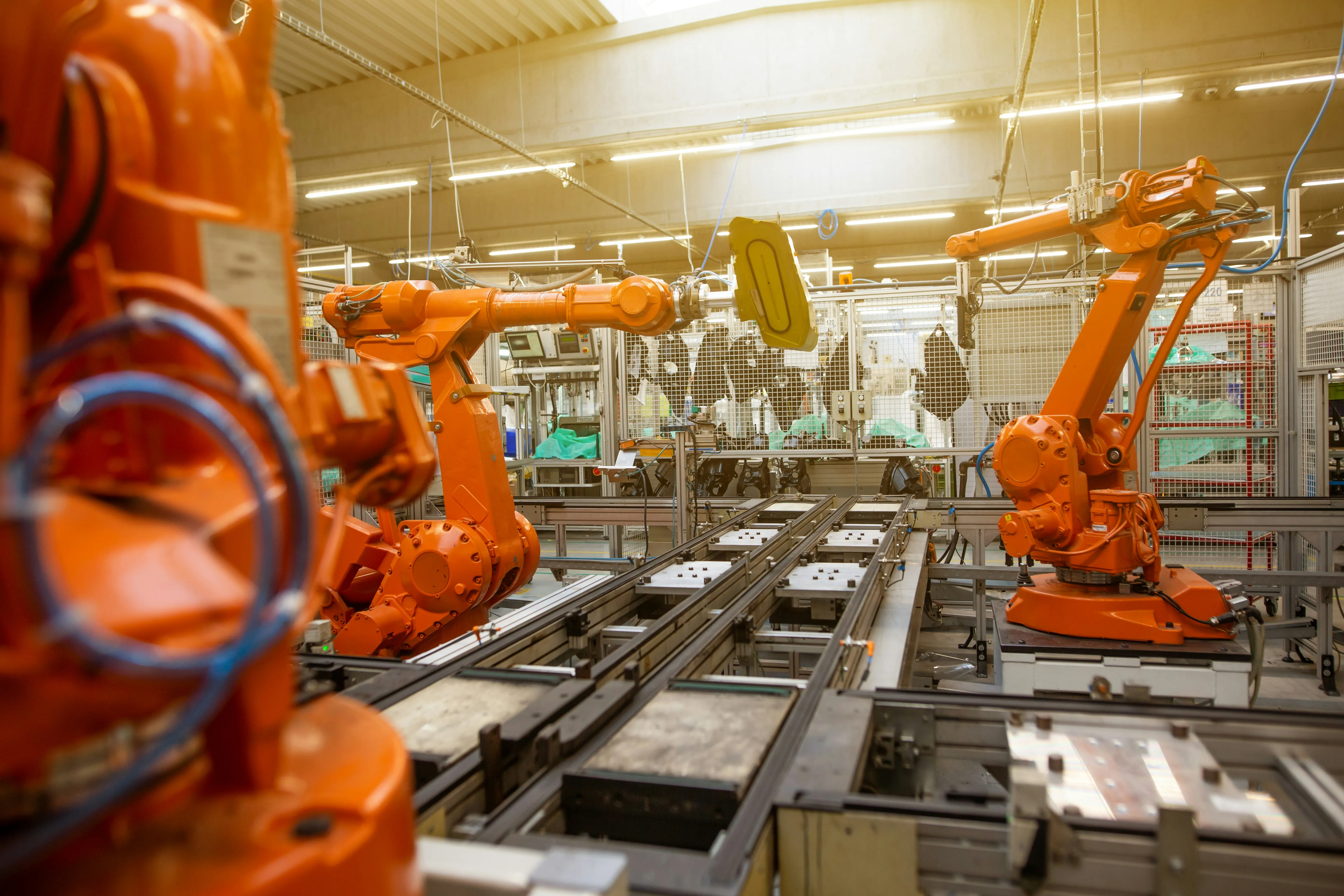 Orange industrial robotic arms operating on an assembly line in a bright manufacturing facility.