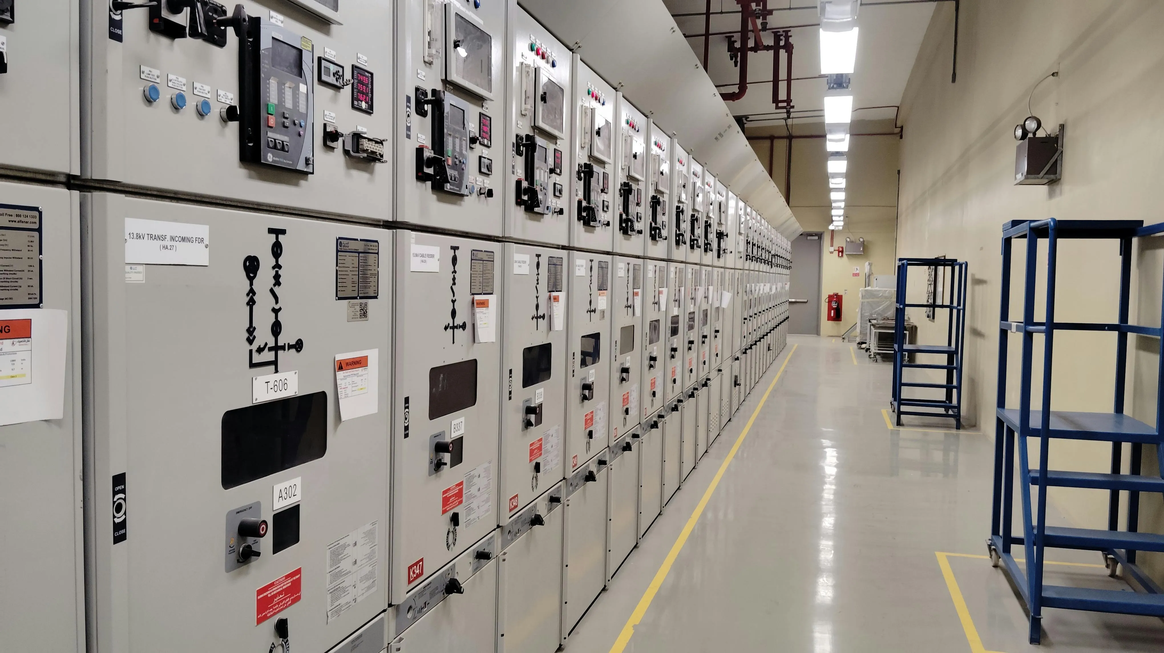 Long row of industrial electrical control panels in a clean utility room with blue metal racks.