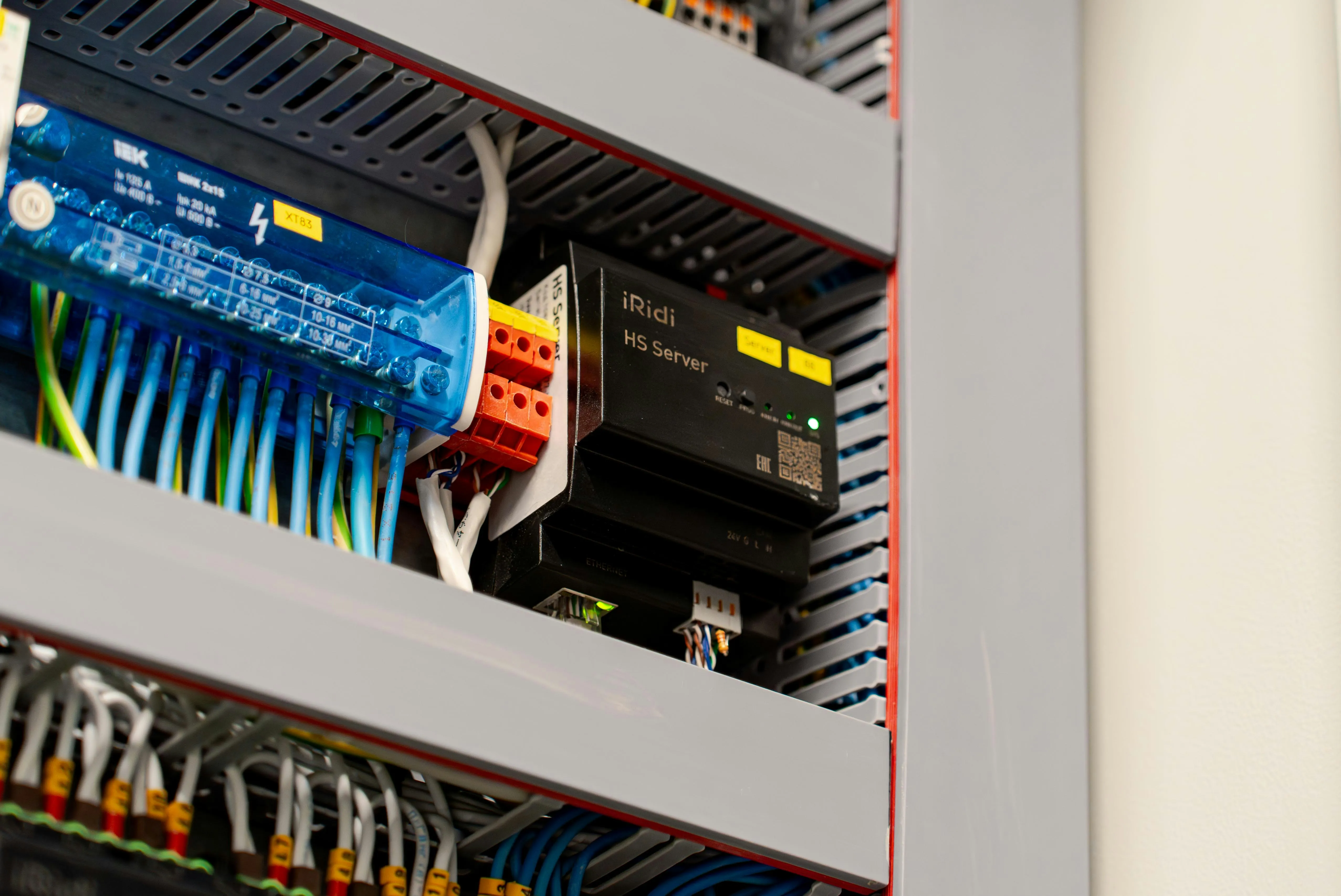 Electrical panel with labeled wiring and an iRidi HS Server device with green indicator lights.