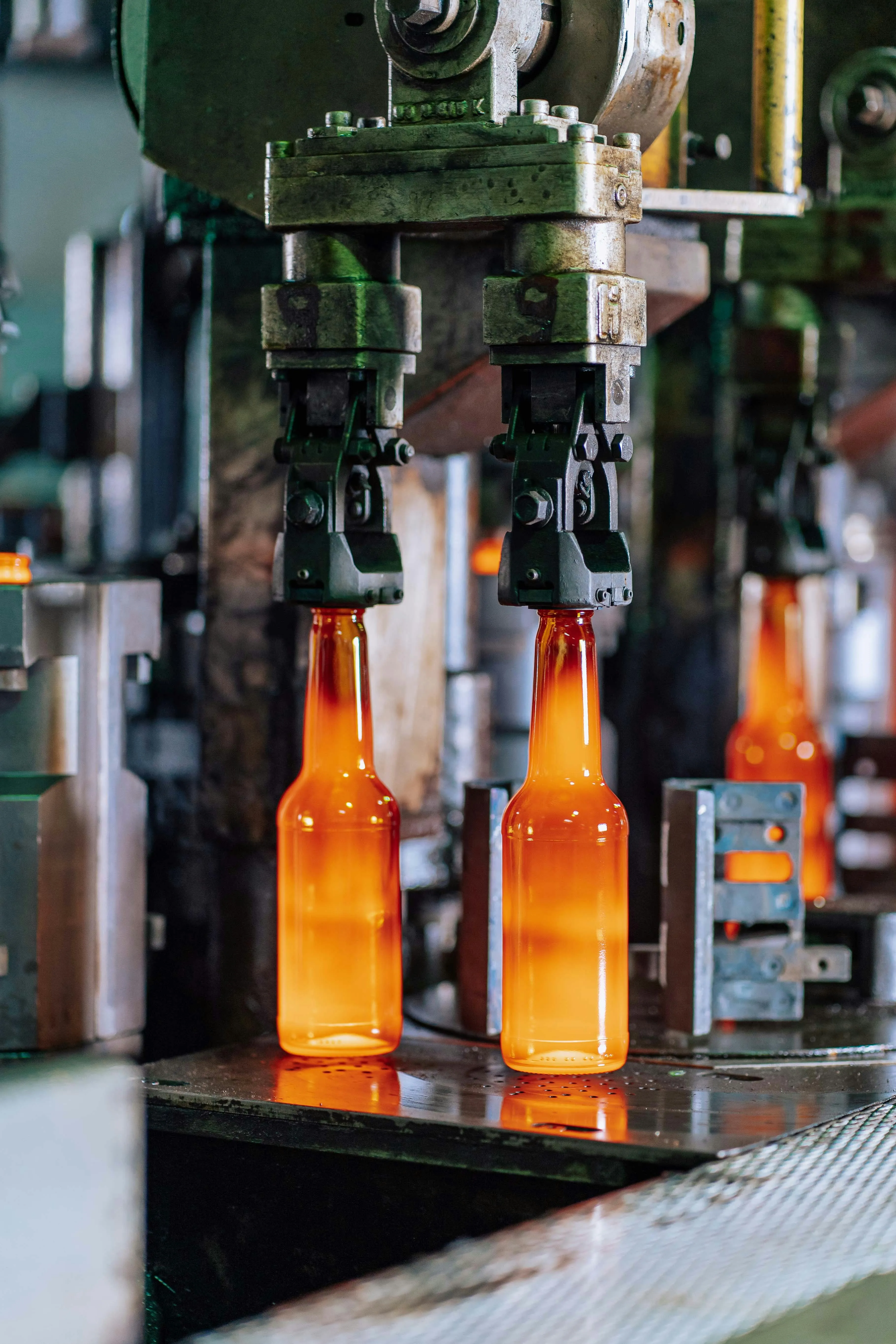 Hot glass bottles being formed and held by mechanical clamps on an industrial production line.