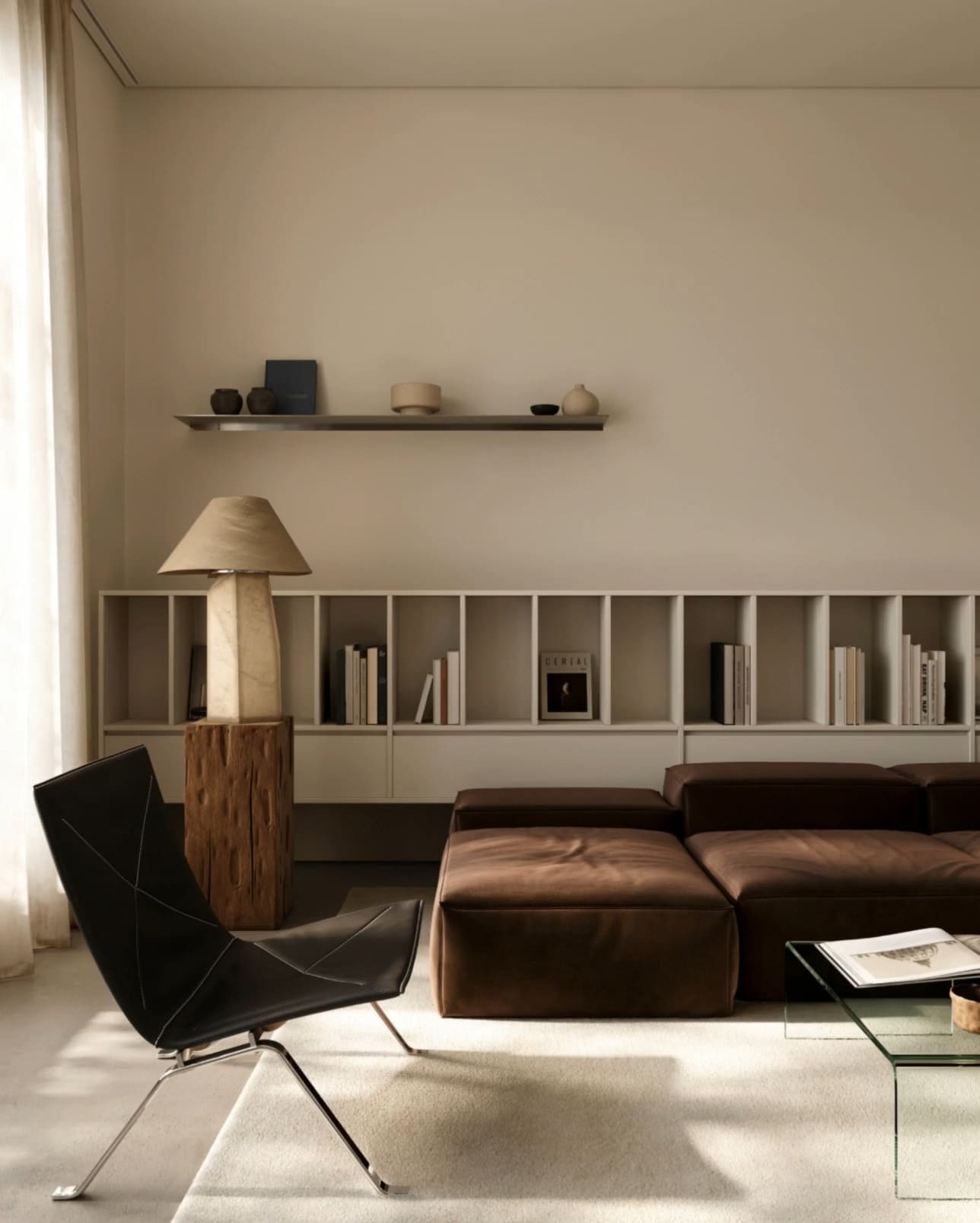 Minimalist living room with brown sectional sofa, glass coffee table, black chair, and shelf with books and decor.