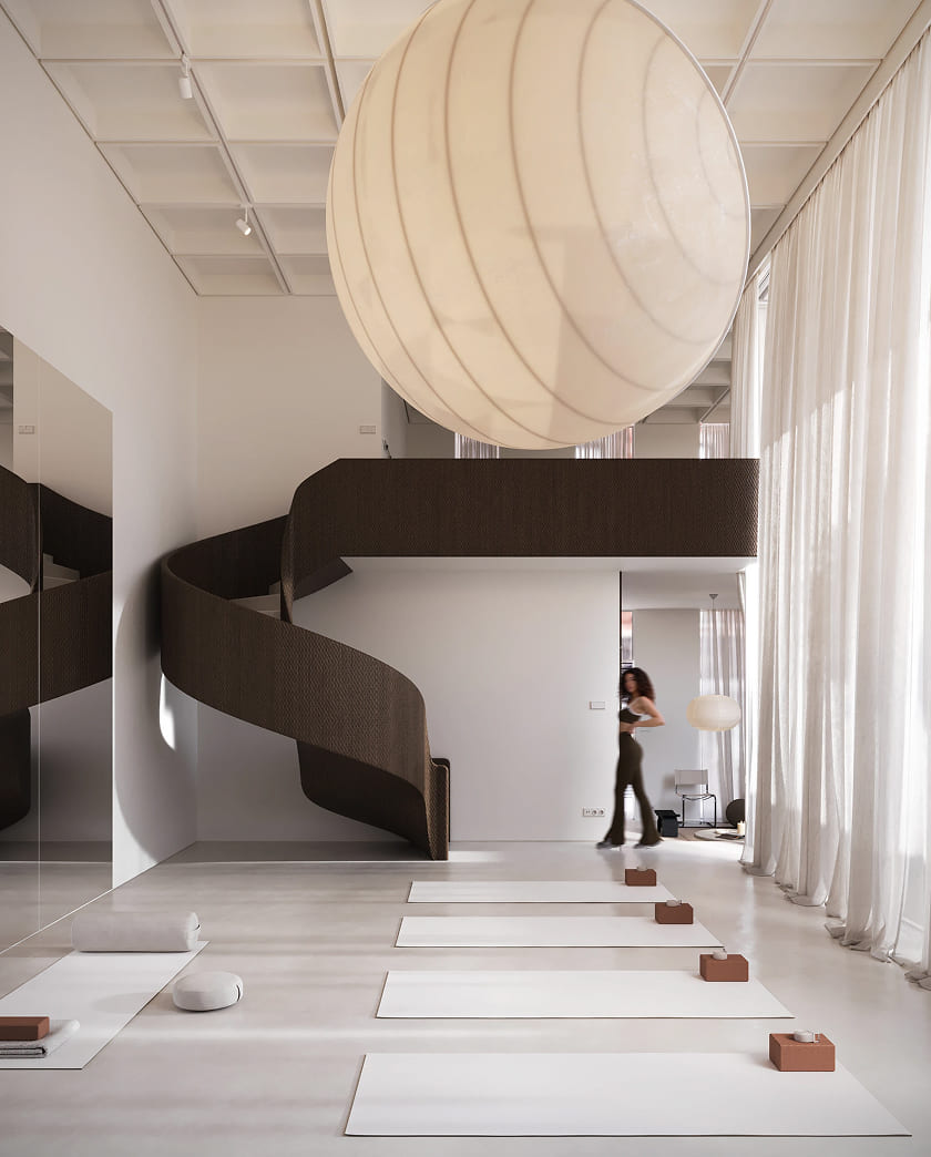 Minimalist yoga studio interior with five white yoga mats lined up on the floor, each accompanied by a brown yoga block and a small candle holder. A large round pendant light hangs from the ceiling. A dark brown spiral staircase leads to an upper level. Floor-to-ceiling sheer curtains cover the windows, and a person wearing a black top and pants walks in the background near a white wall. A large mirror reflects part of the room and staircase.