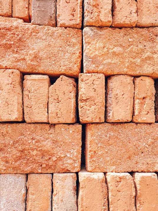 Stacked rows of rough, reddish-orange clay bricks with varied shapes and textures arranged closely together.