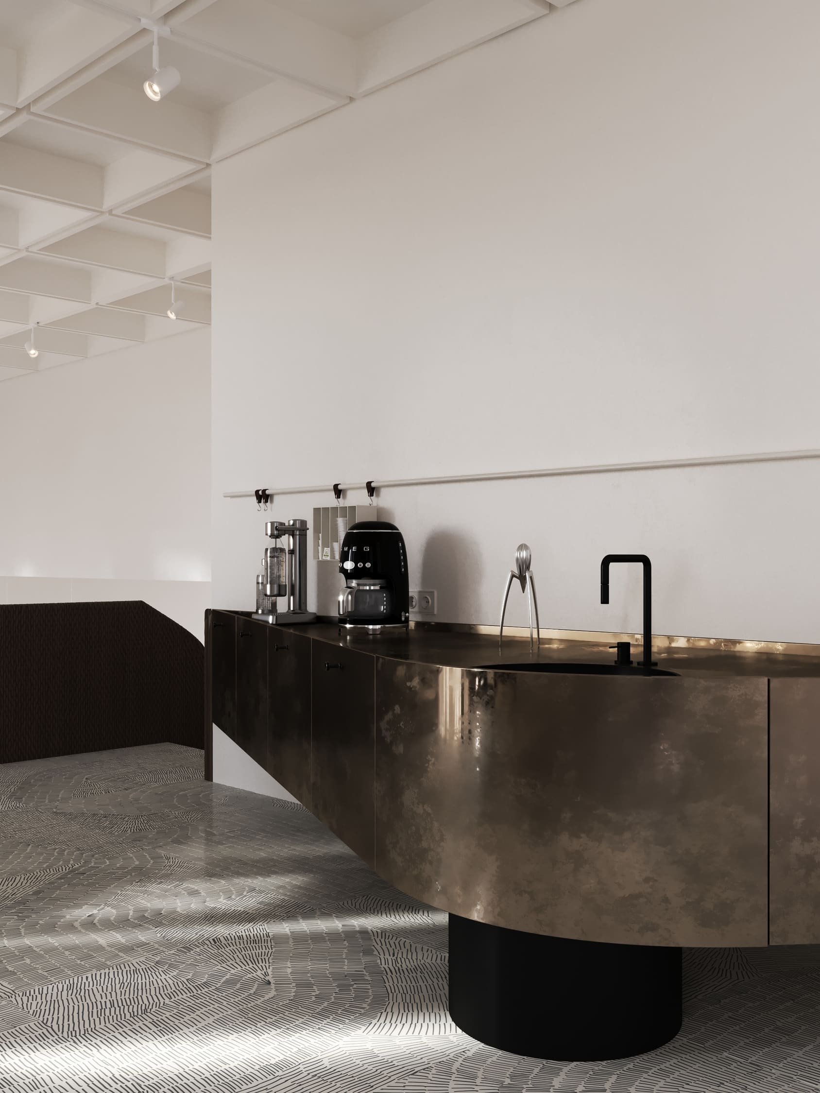 Modern kitchen with a curved dark metallic island featuring a black faucet and sink, a citrus juicer, coffee machine, and a silver appliance on the countertop, against a plain white wall with hanging hooks.