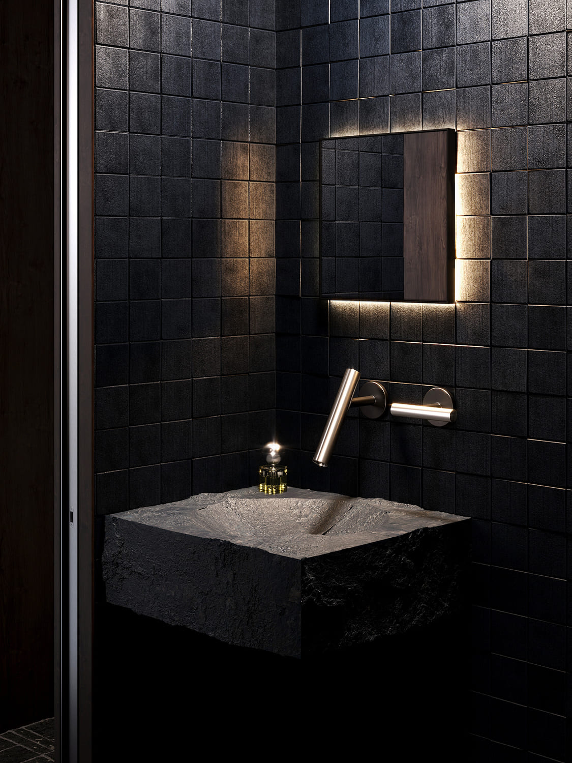 Modern bathroom corner with black textured square tiles, featuring a rough-cut stone sink, a sleek wall-mounted faucet, and a rectangular mirror backlit with soft white light. A small bottle with yellow liquid sits on the sink.