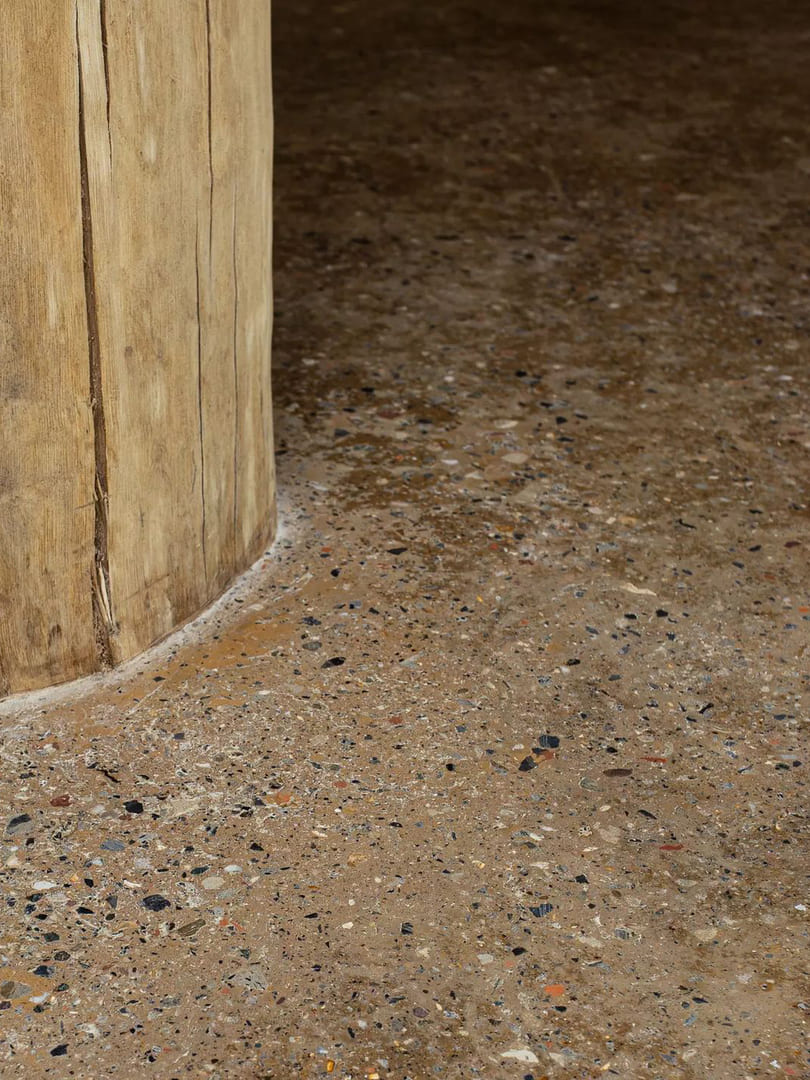 Close-up of a round, natural wood column base set into a polished concrete floor with small exposed aggregate stones.