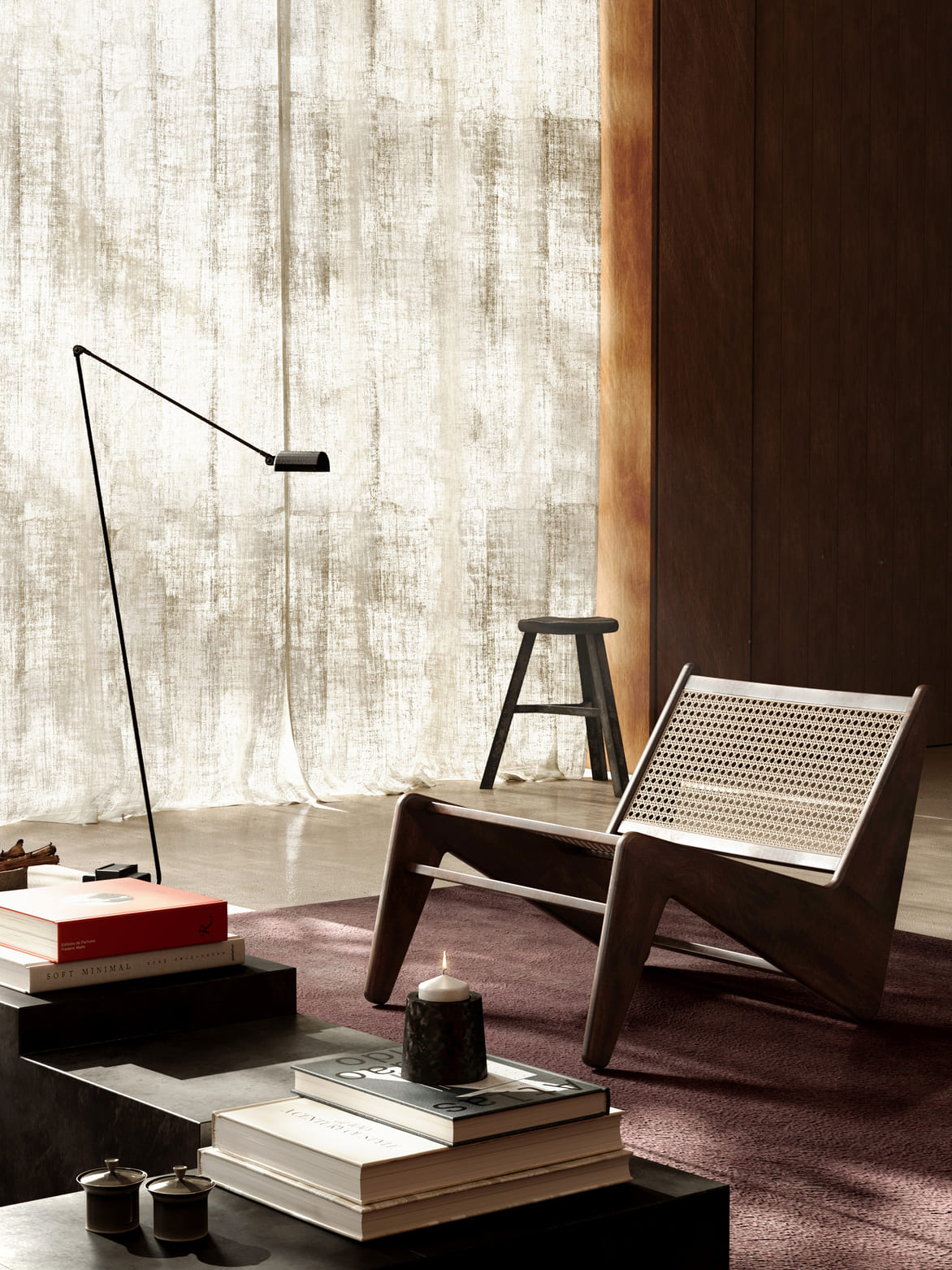 Modern living room corner with a dark wooden lounge chair with woven rattan backrest on a purple rug, a black metal floor lamp, a small black stool near a textured light curtain, and a dark coffee table stacked with books and a lit candle.