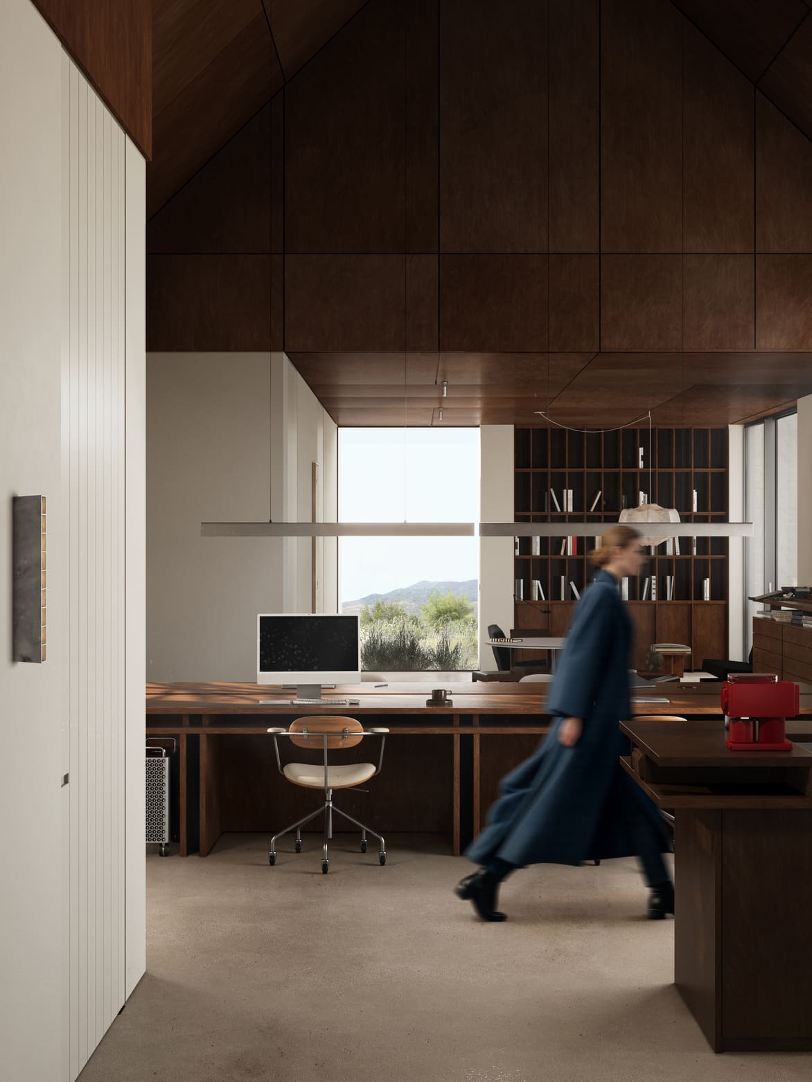 Modern office space with dark wood ceiling and furniture, a large desk with a chair and computer, a large window showing outdoor greenery and mountains, and a person in a long blue coat walking blurred through the room.