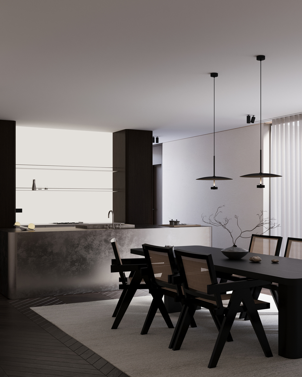 Modern dining area with a dark rectangular table surrounded by six black wooden chairs with mesh backs on a light rug, next to a minimalist kitchen island with a metallic finish and a sink; two pendant lights hang from the ceiling, and a decorative vase with bare branches sits on the table; sheer floor-to-ceiling curtains cover the window, and the color scheme is mainly monochromatic with soft natural lighting.