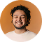 Smiling man with curly hair and a beard wearing a white shirt against an orange background.