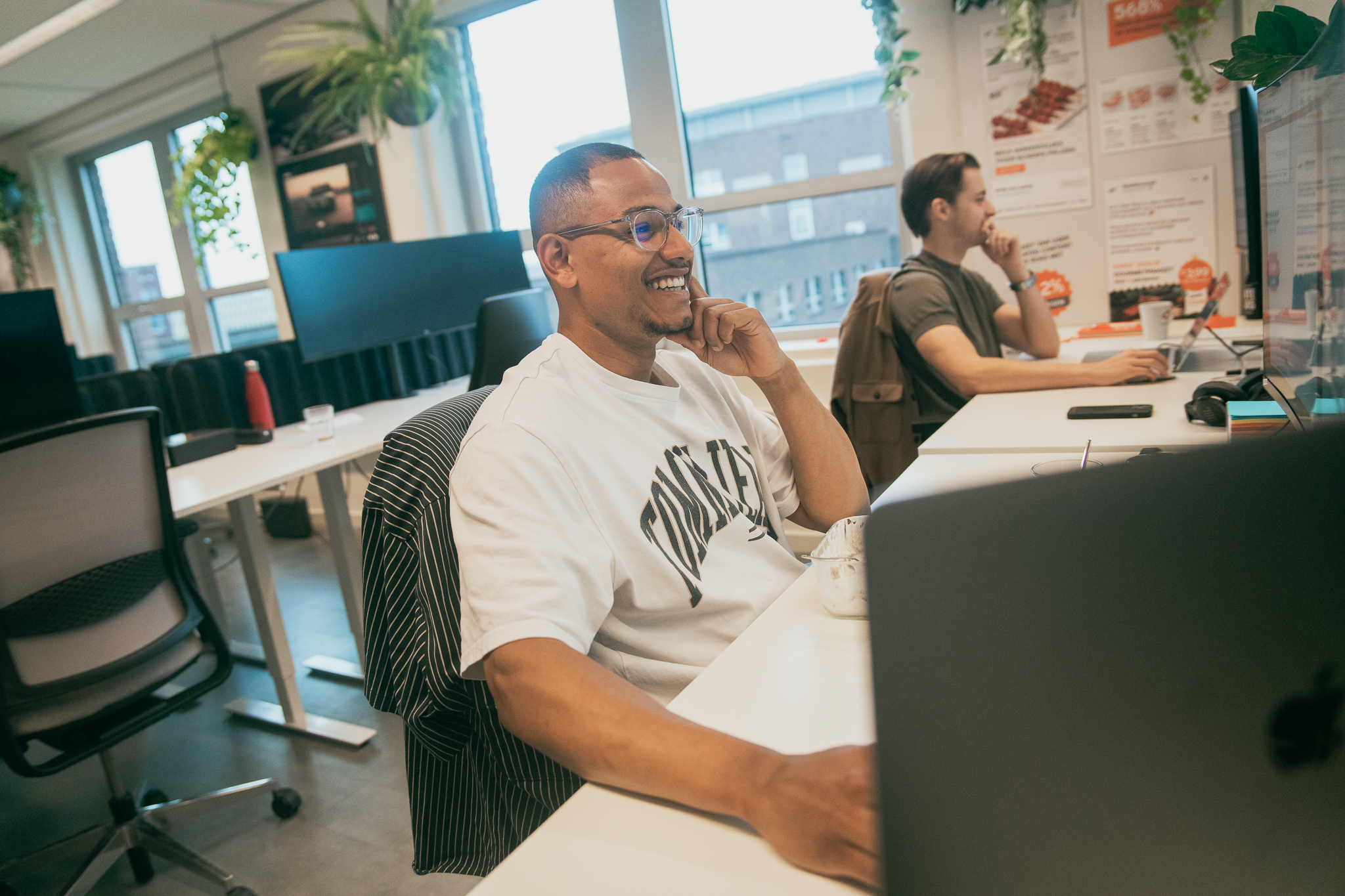 Two men working on laptops in a bright modern office with plants and windows.